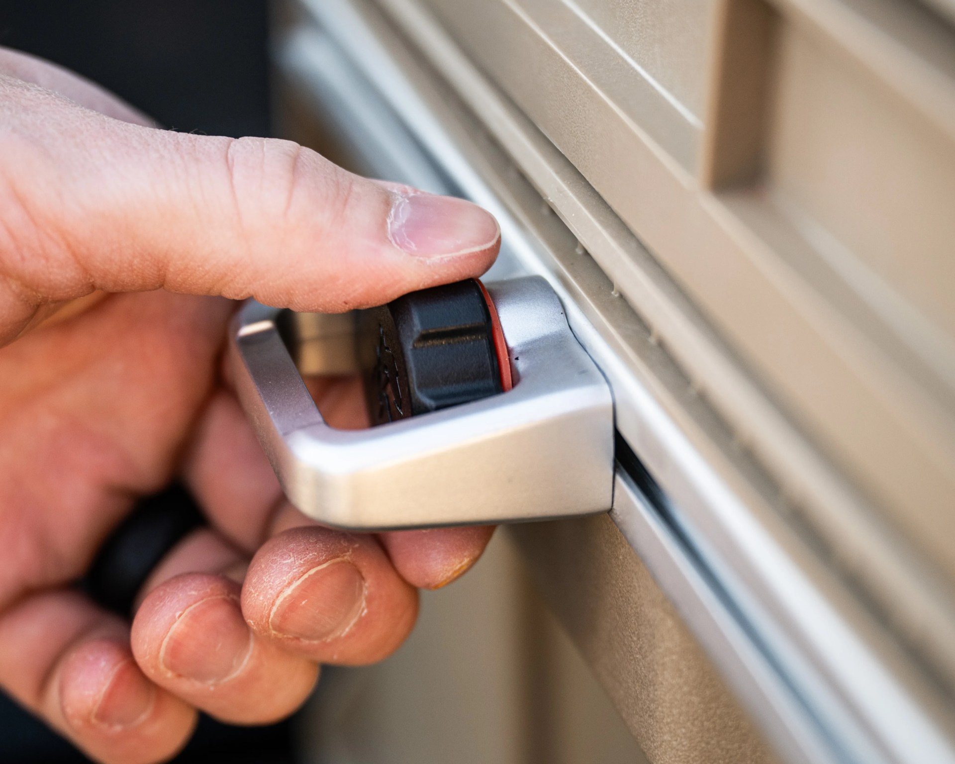 Hand gripping a silver and black latch on a beige surface.