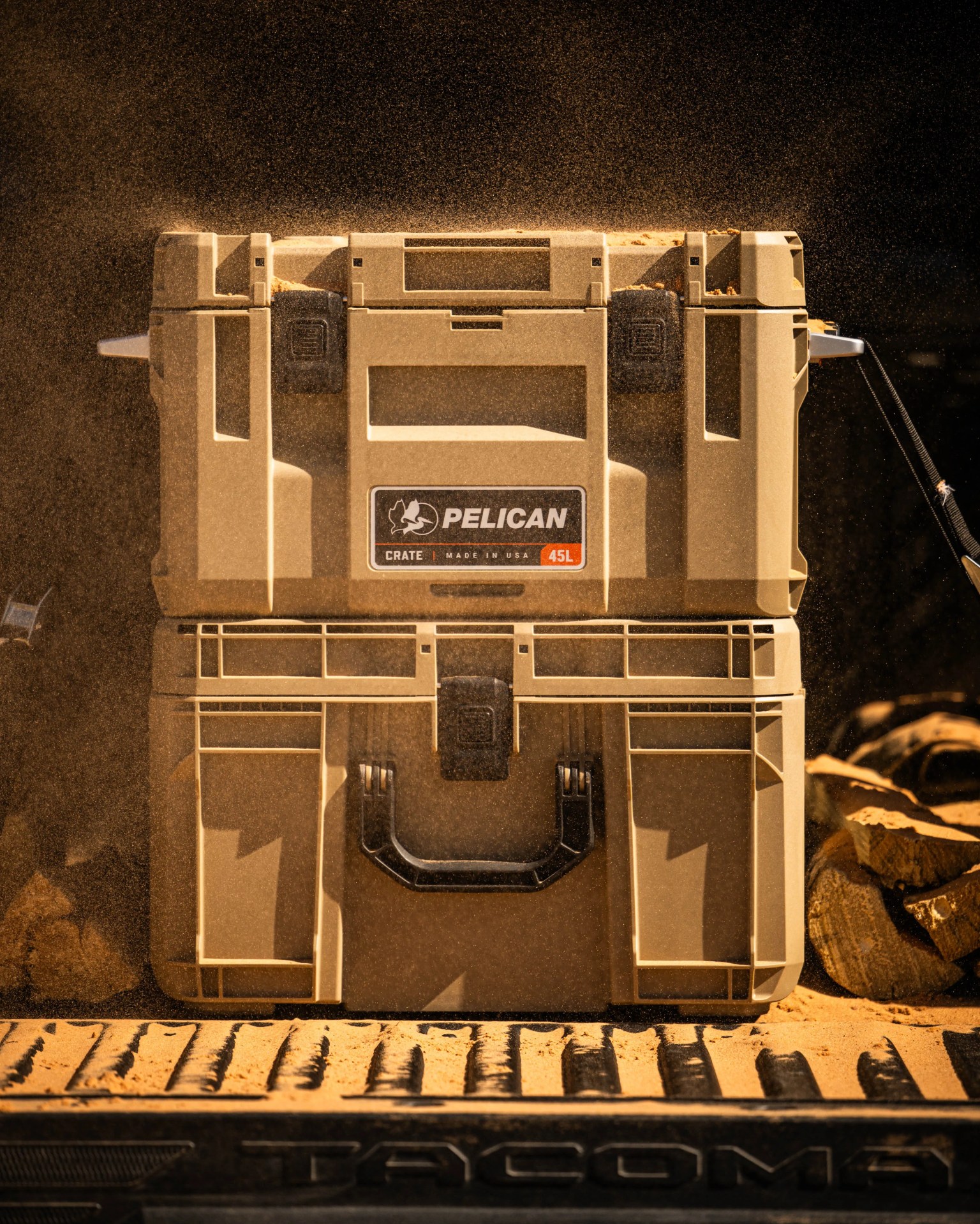 Tan Pelican 45L crate with black latches and handle, filled with sand, on a truck bed with "Tacoma" text.
