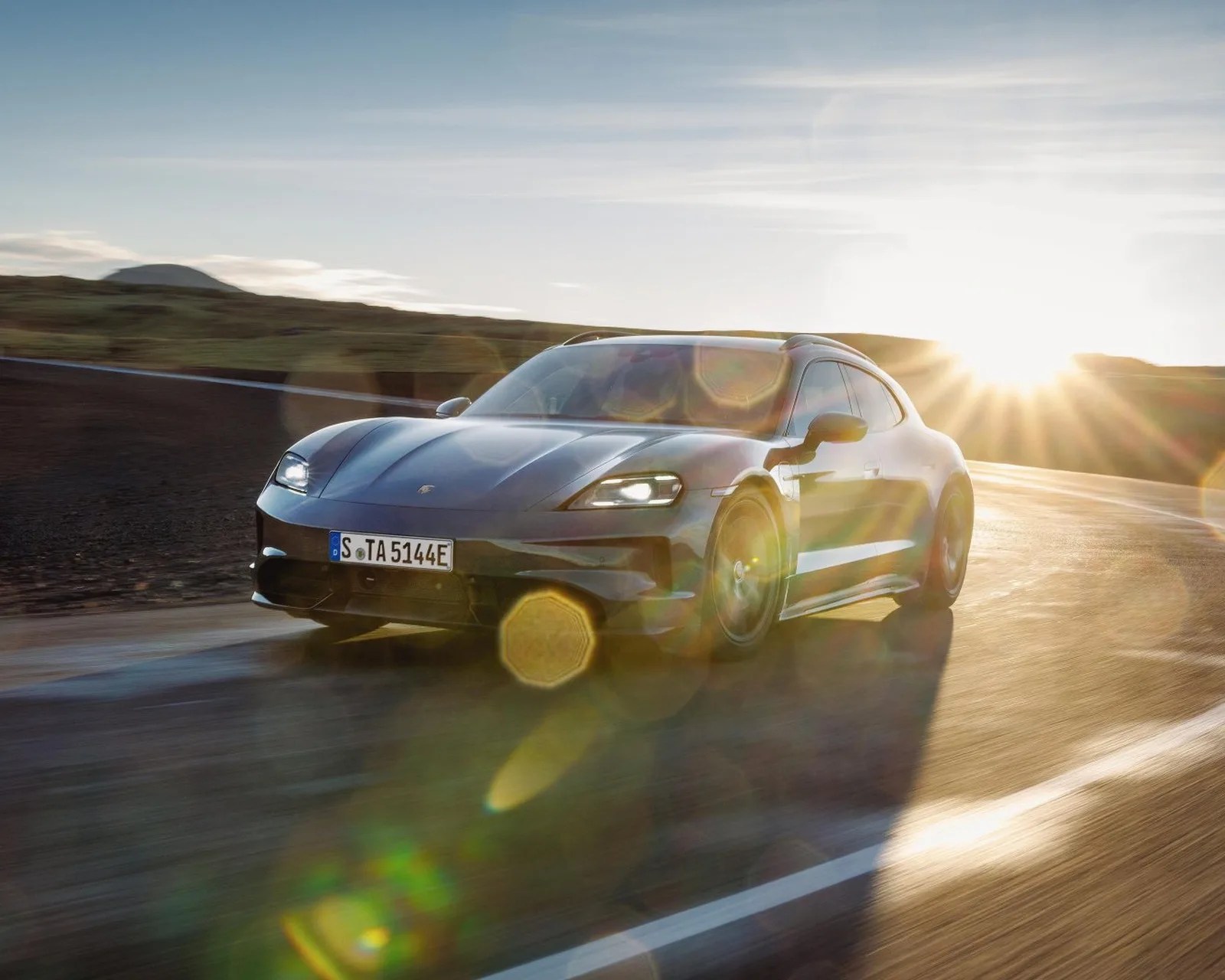 Black Porsche Taycan driving on a curved road with sun glare in the background.