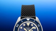 Close-up of a Seiko watch with a blue dial, luminous markers, and a textured black rubber strap.