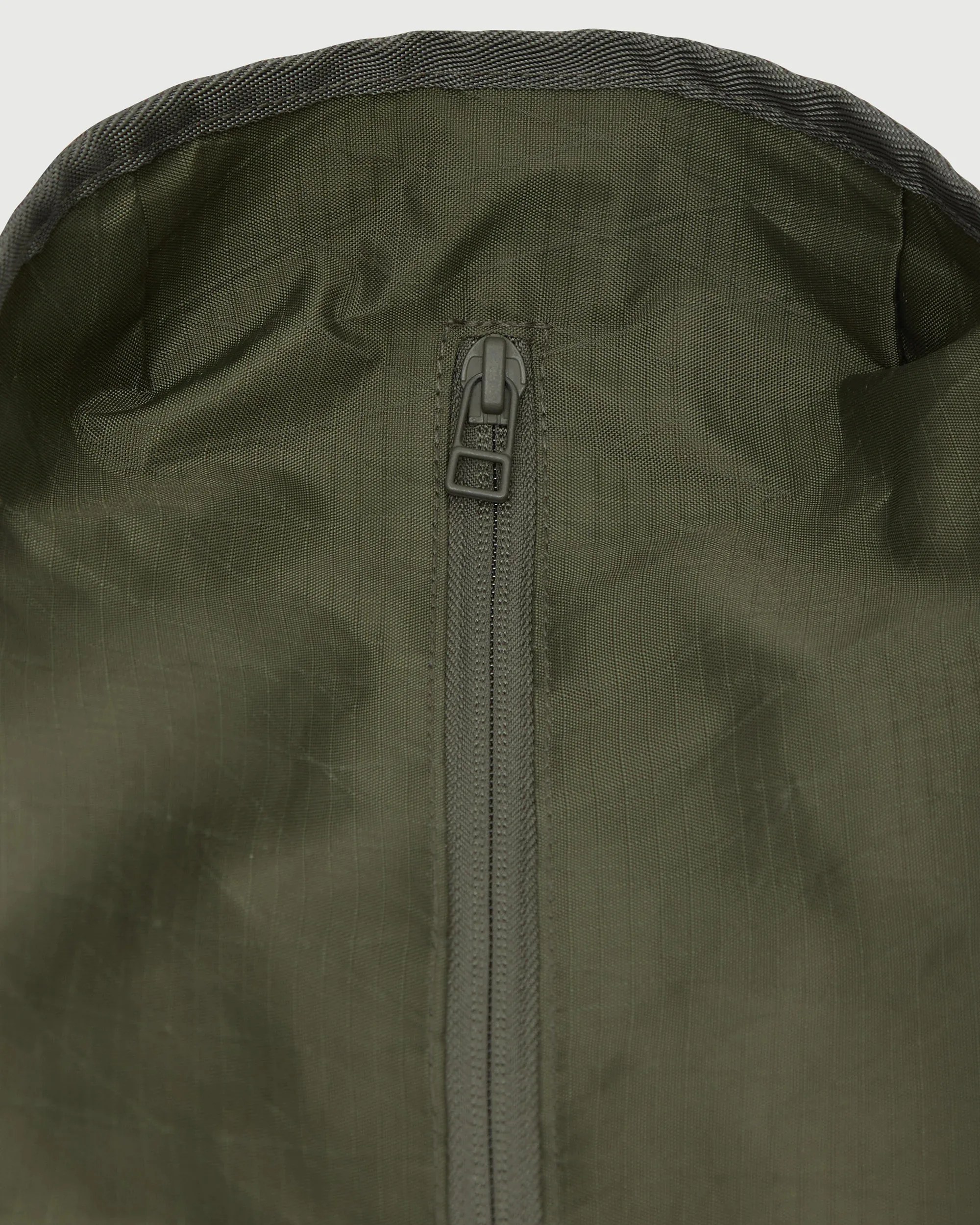 Close-up of an olive green fabric with a centered zipper and black trim along the edge.