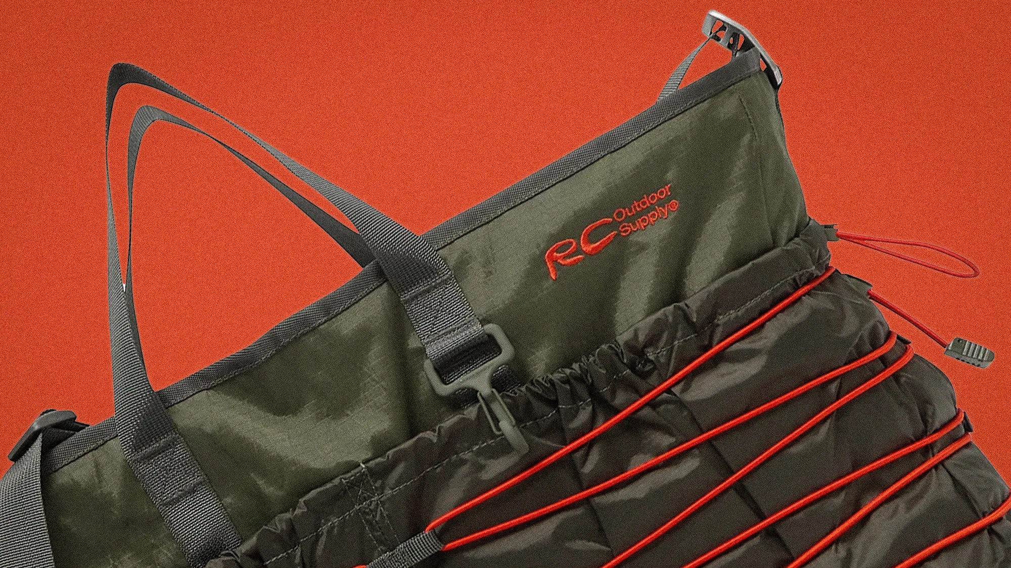Olive green RC Outdoor Supply bag with black straps and red elastic cords on an orange background.