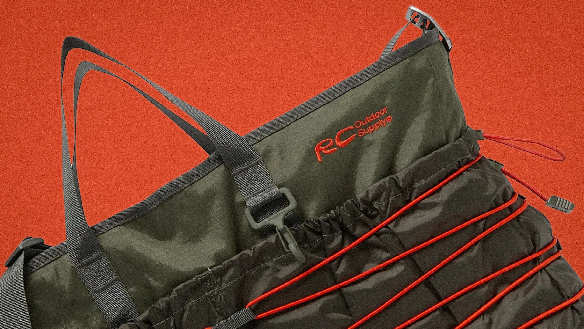 Olive green RC Outdoor Supply bag with black straps and red elastic cords on an orange background.