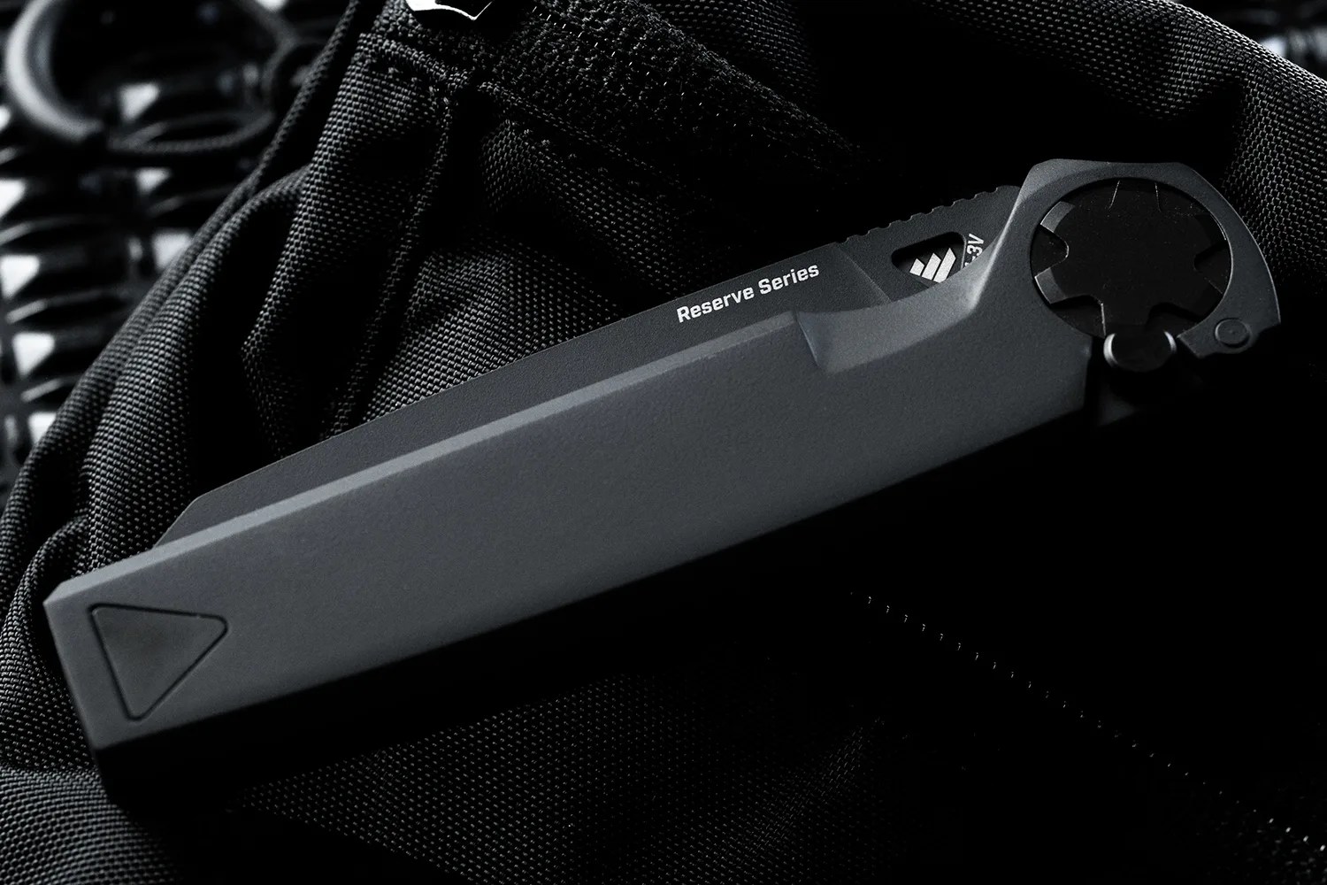 Black folding knife with "Reserve Series" text on the blade, resting on black textured fabric.