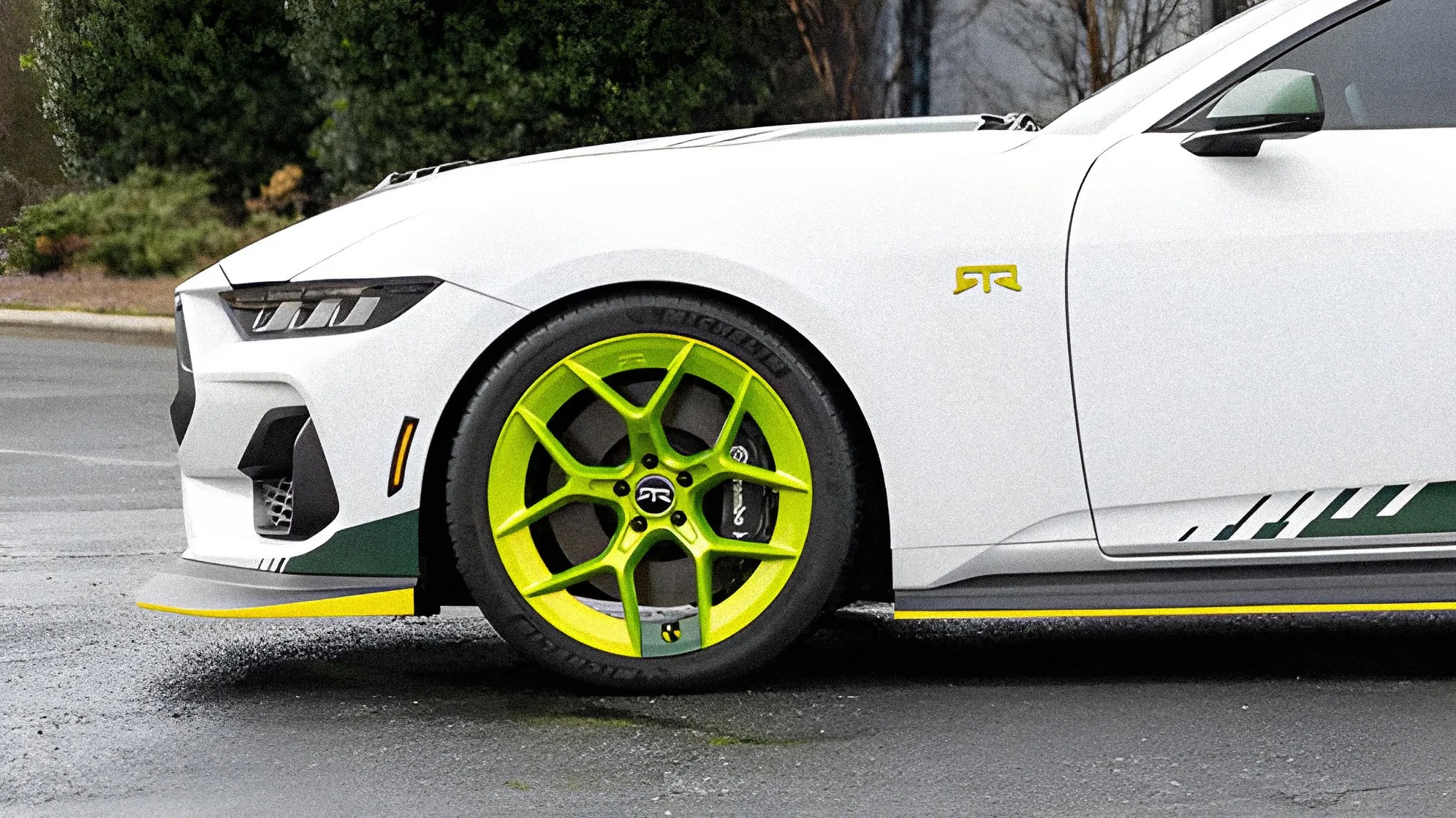White sports car front side with neon green wheel and yellow-accented splitter on asphalt.