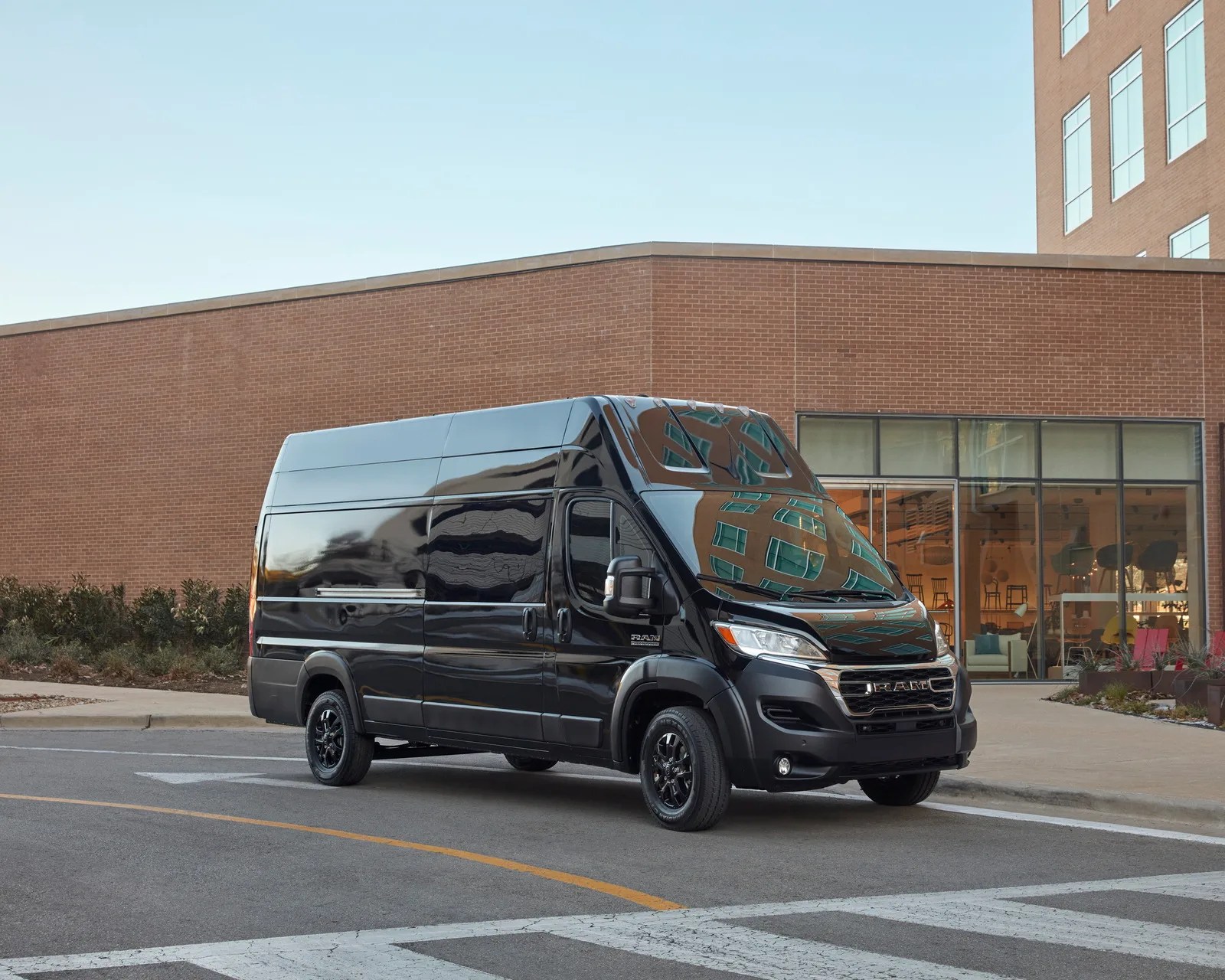 Black high-roof RAM cargo van parked on a street in front of a brick building with large windows.
