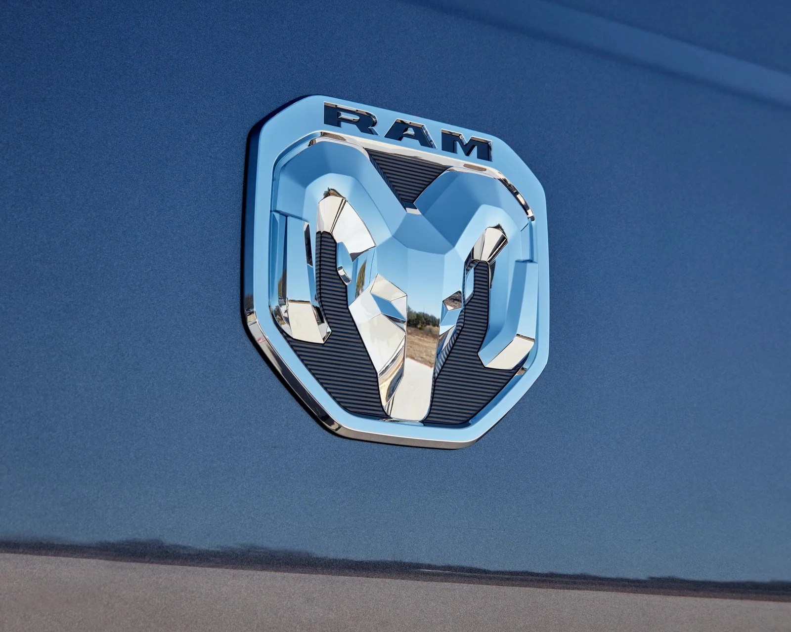 Chrome RAM emblem with ram head design on blue vehicle surface.