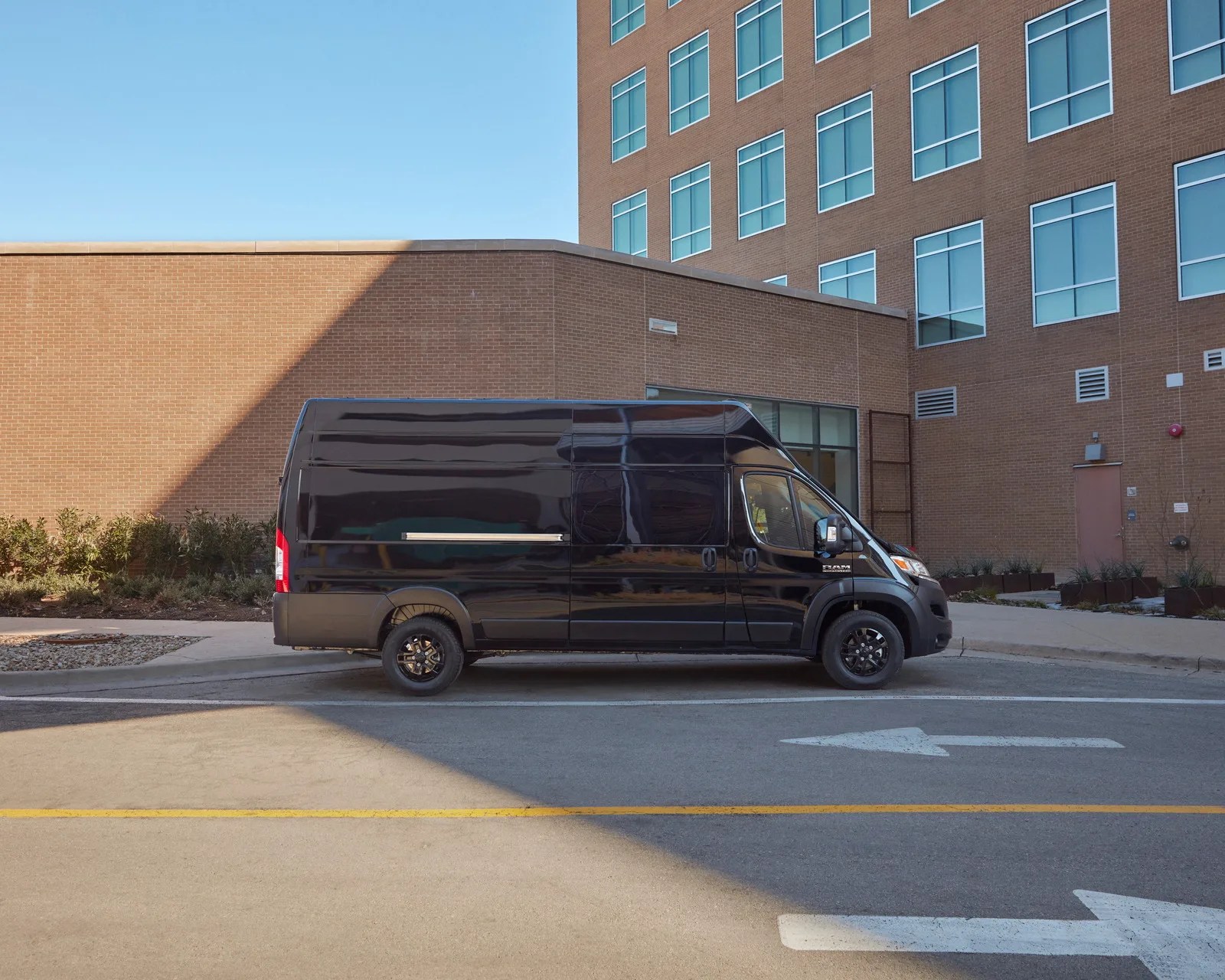 Black high-roof cargo van parked on a street beside a brick building with multiple windows.