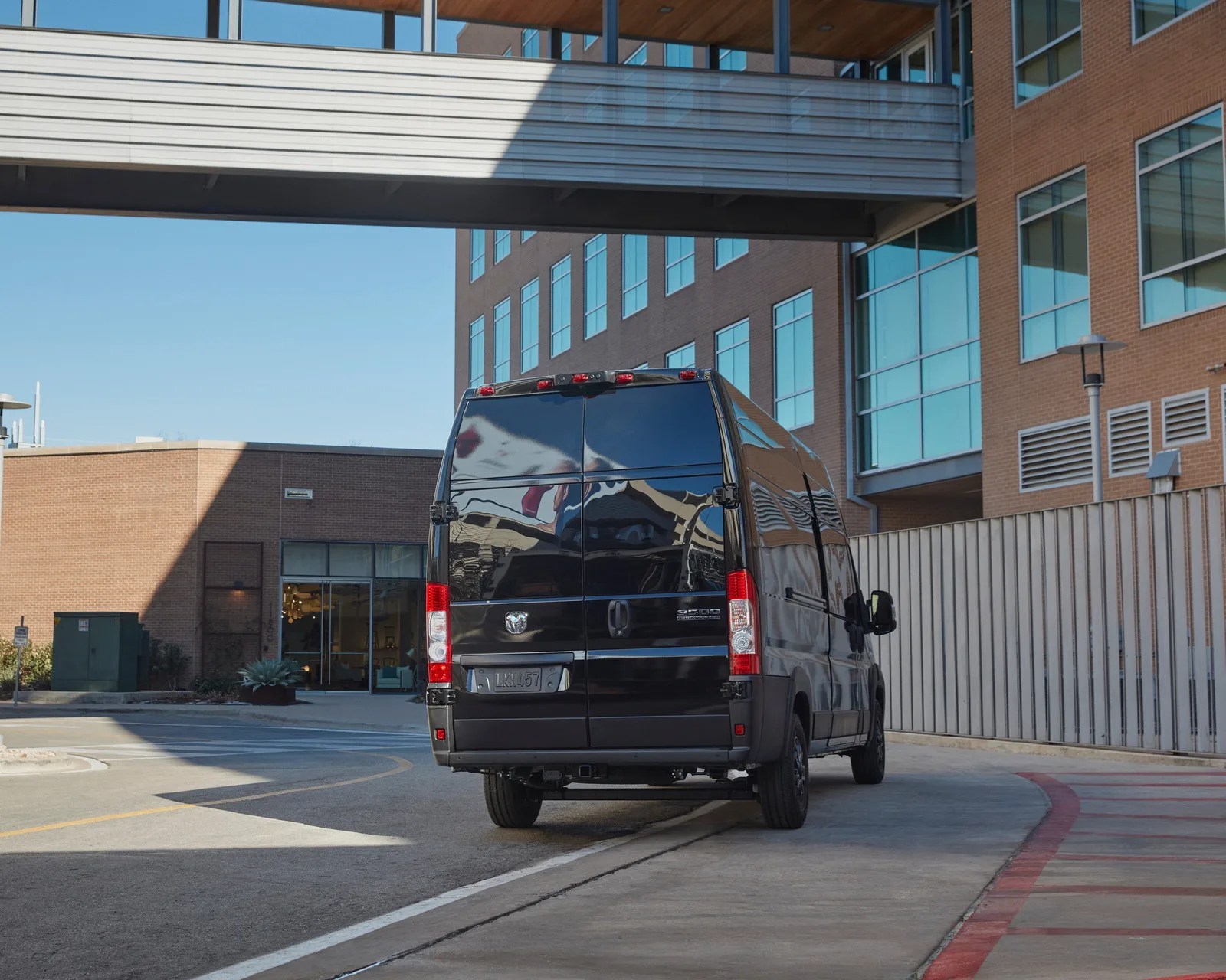 Black Ram 3500 ProMaster van parked on a curved driveway near a brick building with large windows.