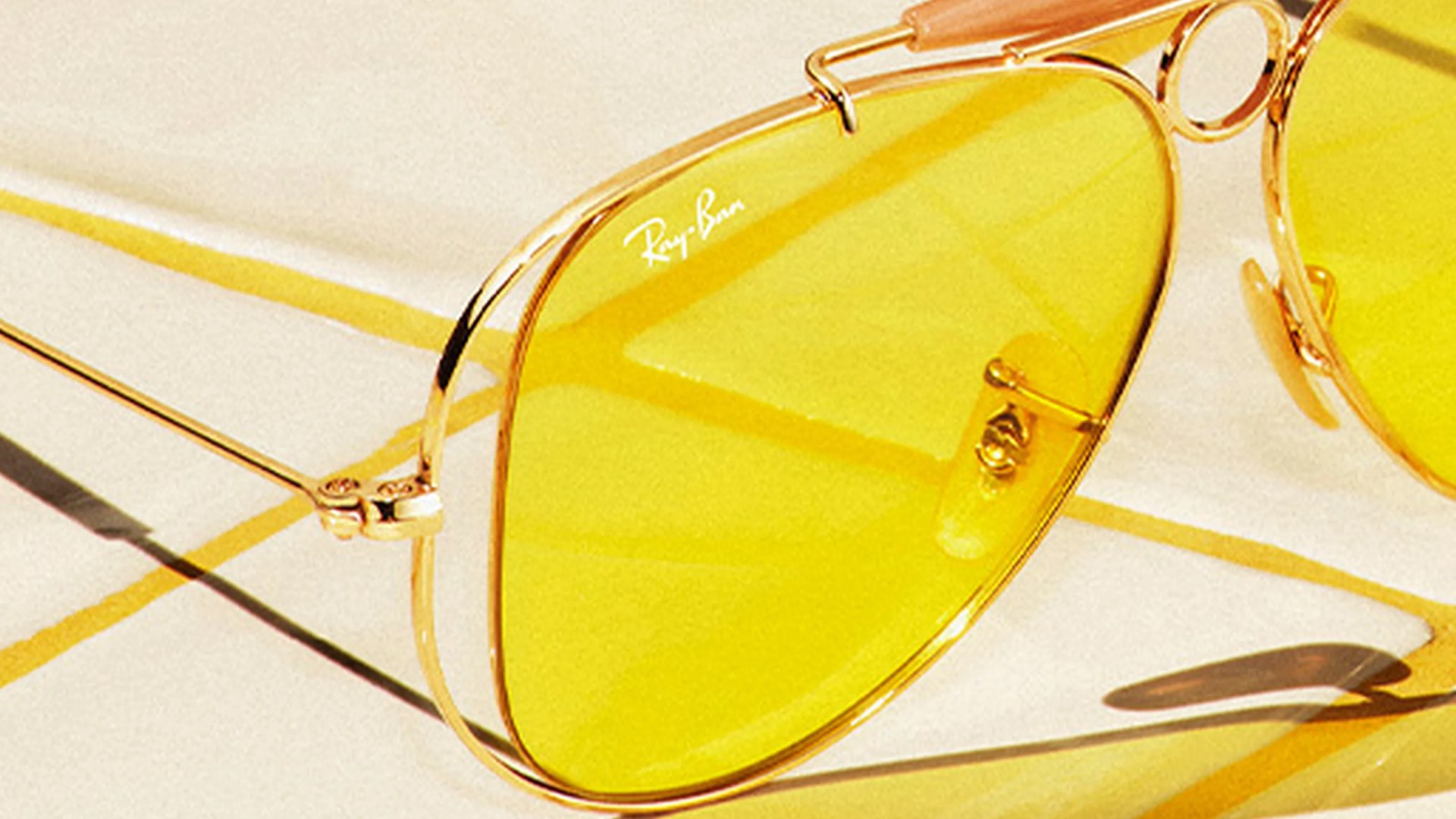Gold-framed Ray-Ban aviator sunglasses with yellow lenses on a light surface.