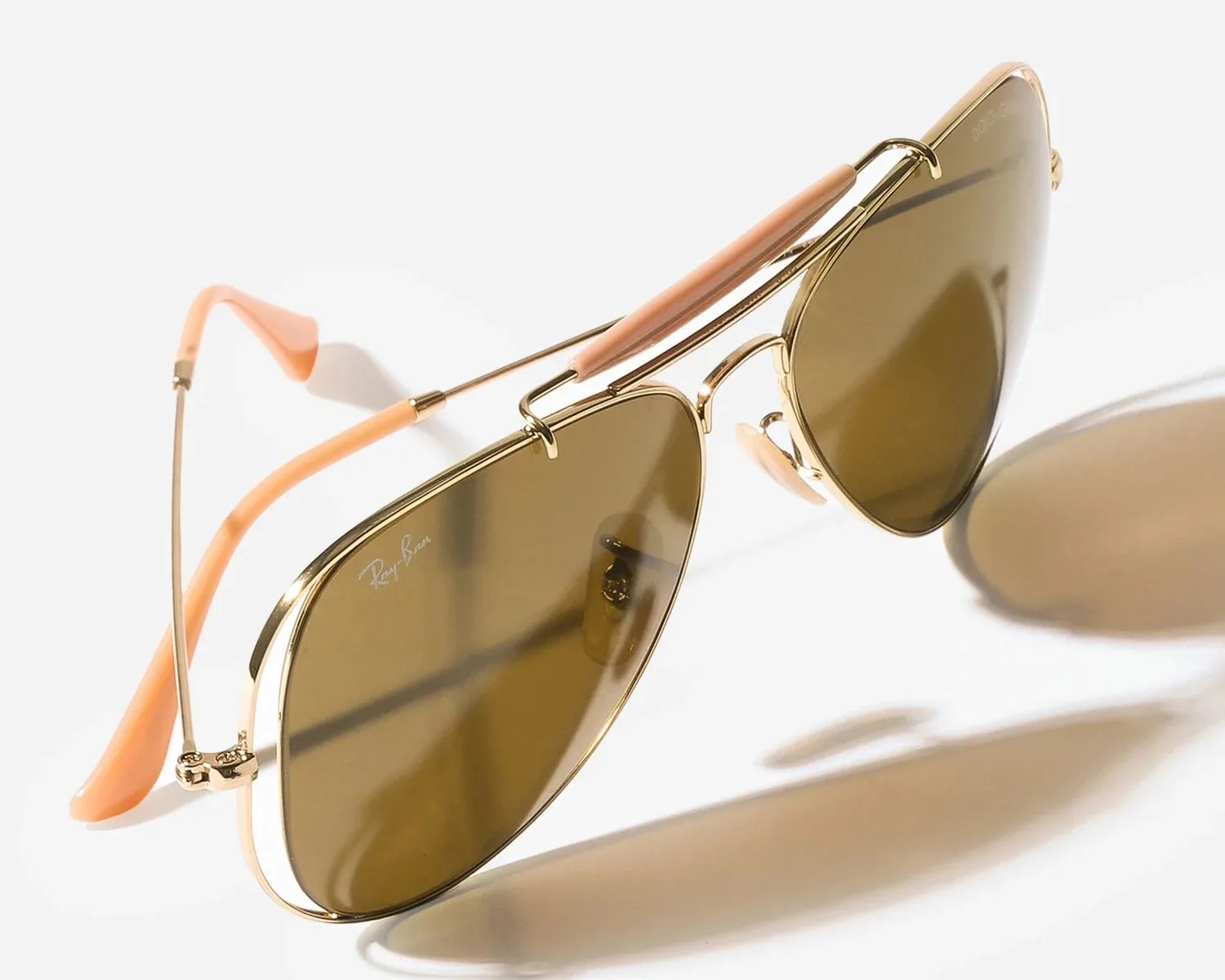 Gold-framed aviator sunglasses with brown lenses and peach-colored temple tips and nose pads.
