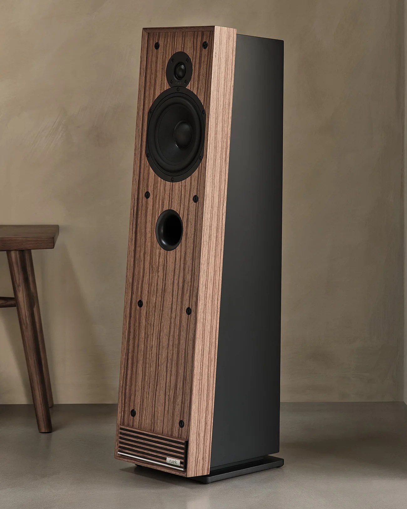 Tall floor-standing speaker with wood grain front panel and black sides on a gray floor.