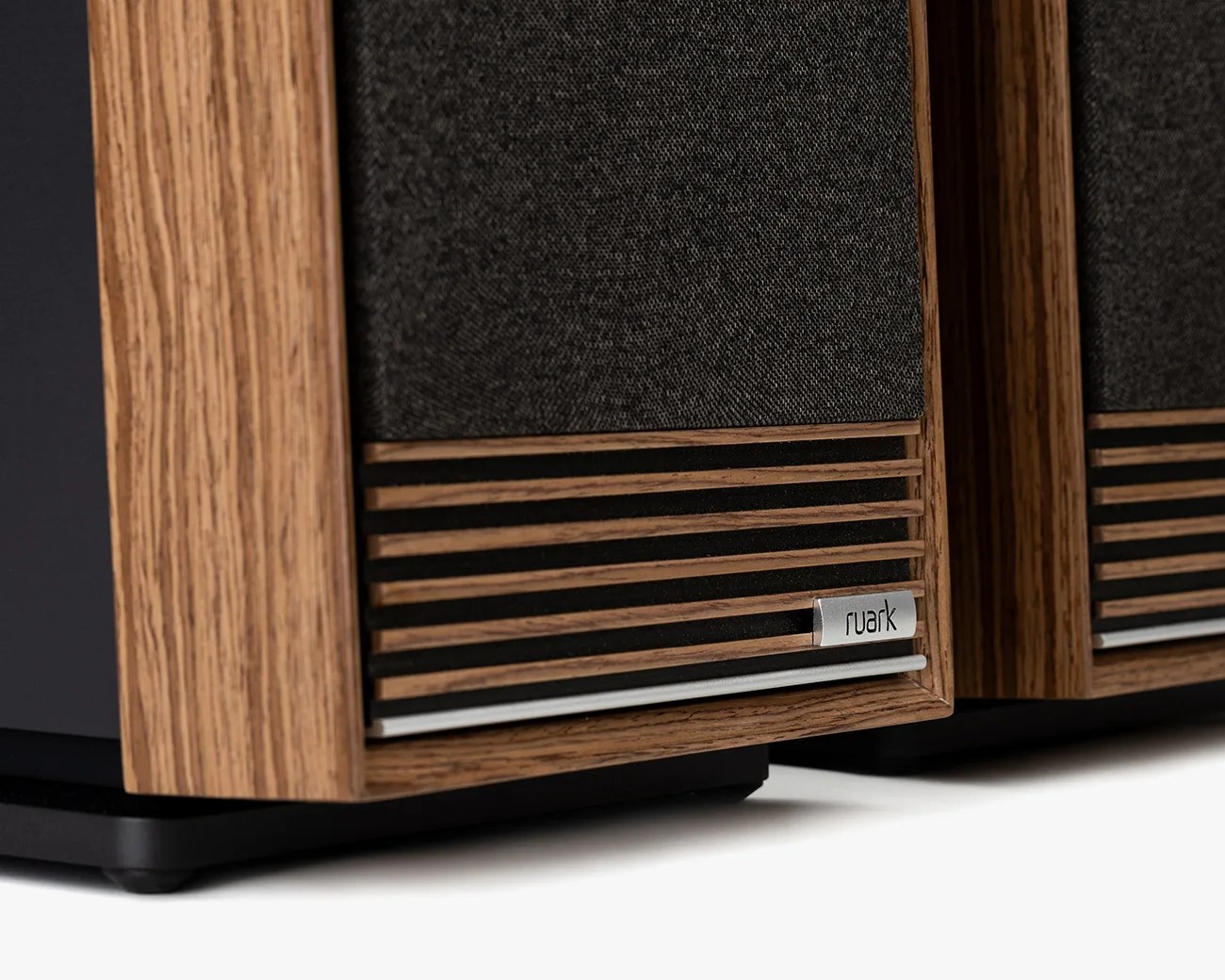 Close-up of a wooden-framed speaker with black fabric grille and "ruark" metal logo plate.