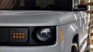 Close-up of a white vehicle's front left headlight and amber side marker light with a black grille section.