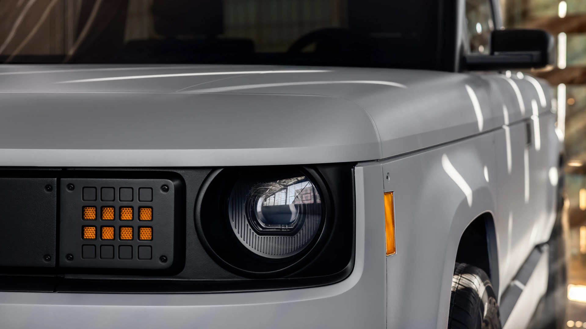 Close-up of a white vehicle's front left headlight and amber side marker light with a black grille section.