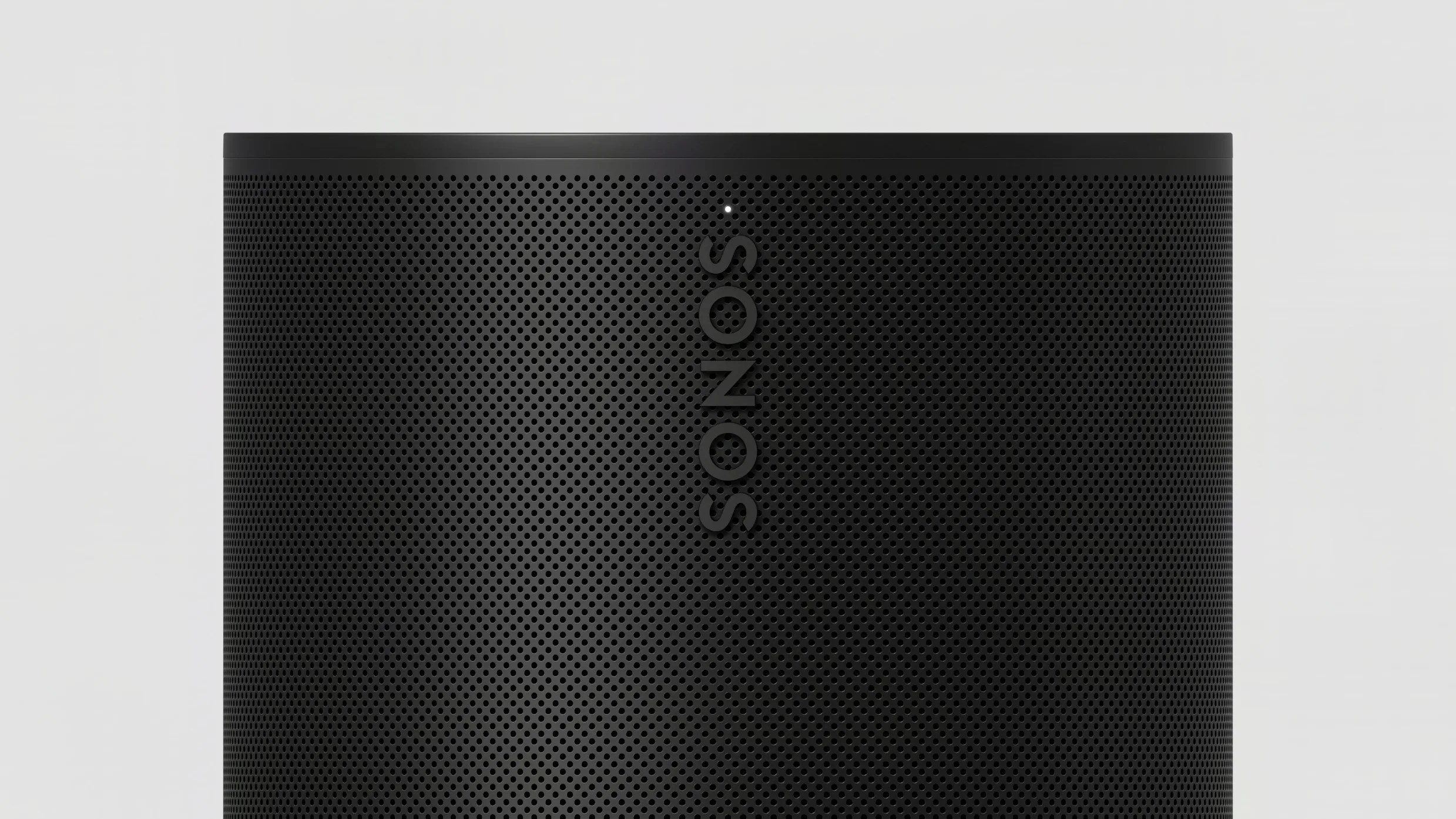 Close-up of a black Sonos speaker grille with perforated holes and a small white indicator light.