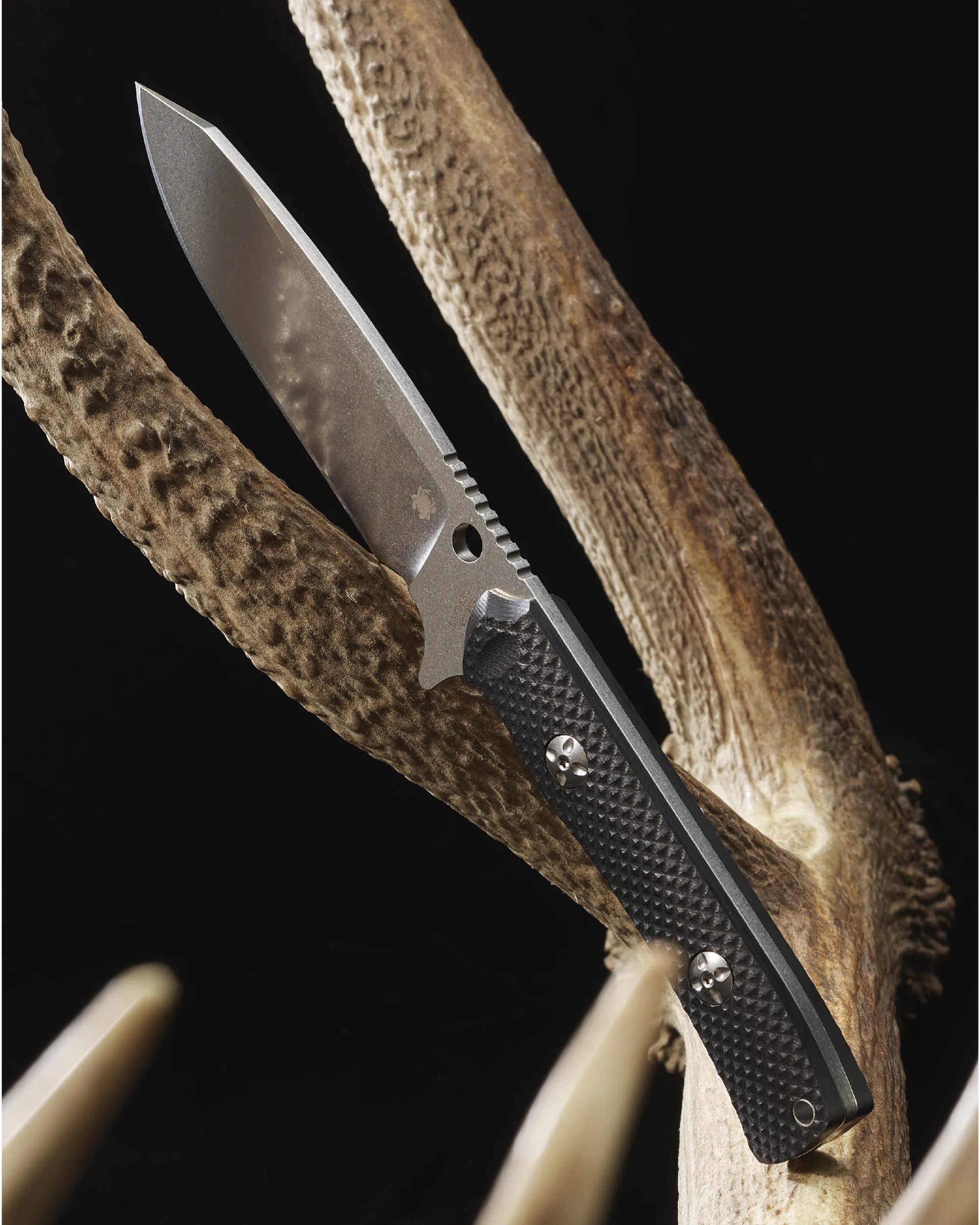 Stonewashed fixed blade knife with textured black handle resting on a brown antler against a black background.