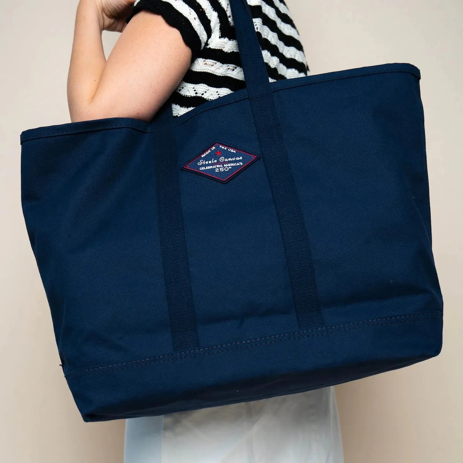 Navy blue canvas tote bag with long handles and a diamond-shaped patch worn over a shoulder.
