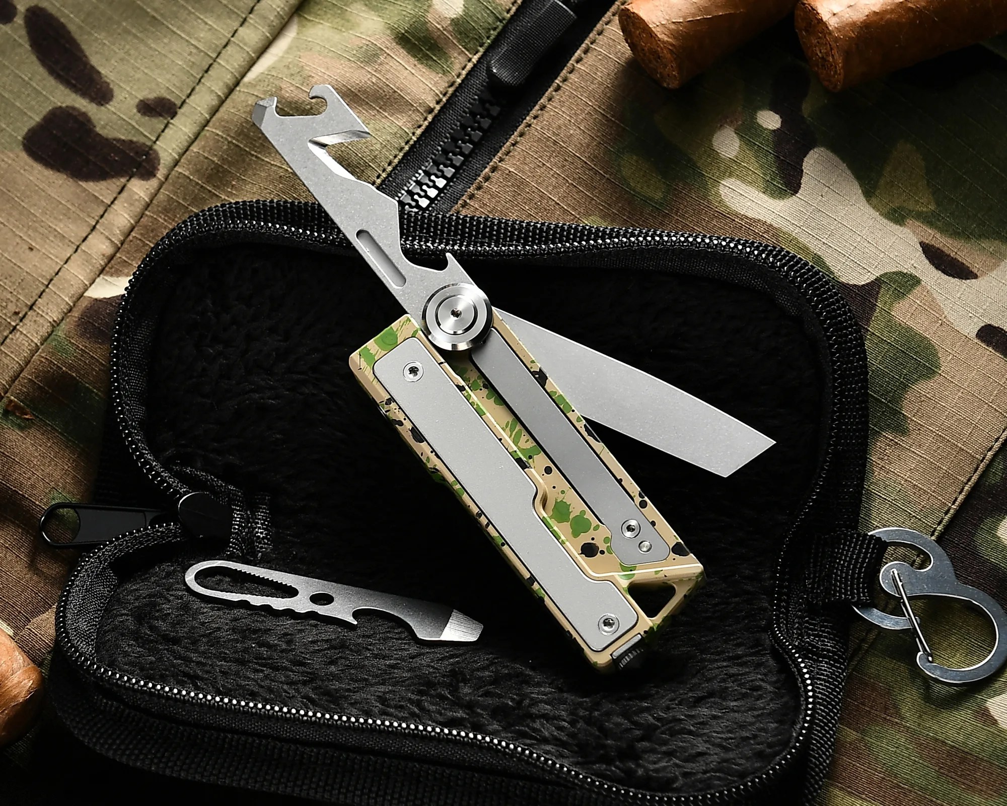 Camouflage-patterned butterfly knife with silver blades and a multi-tool inside a black zippered case on camouflage fabric.