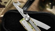 Silver multi-tool with camouflage handle resting on black fabric inside a zippered case on camouflage fabric.