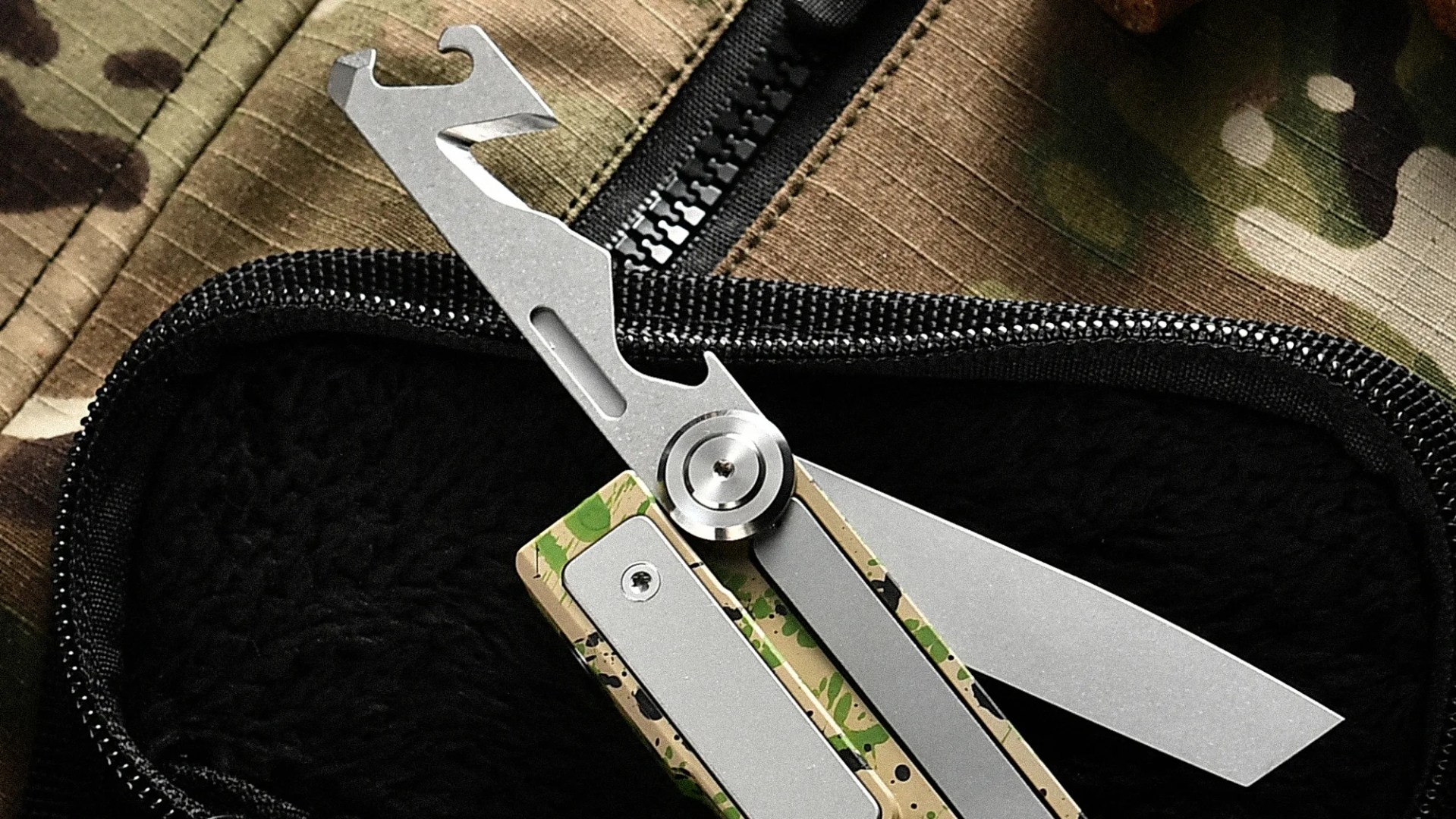 Silver multi-tool with camouflage handle resting on black fabric inside a zippered case on camouflage fabric.