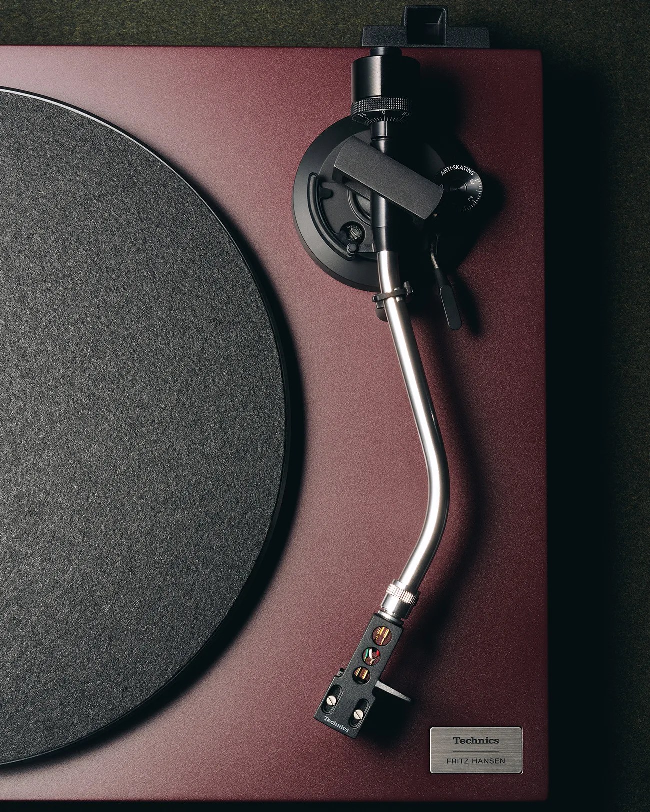 Close-up of a burgundy Technics turntable with a silver tonearm and black felt platter mat.