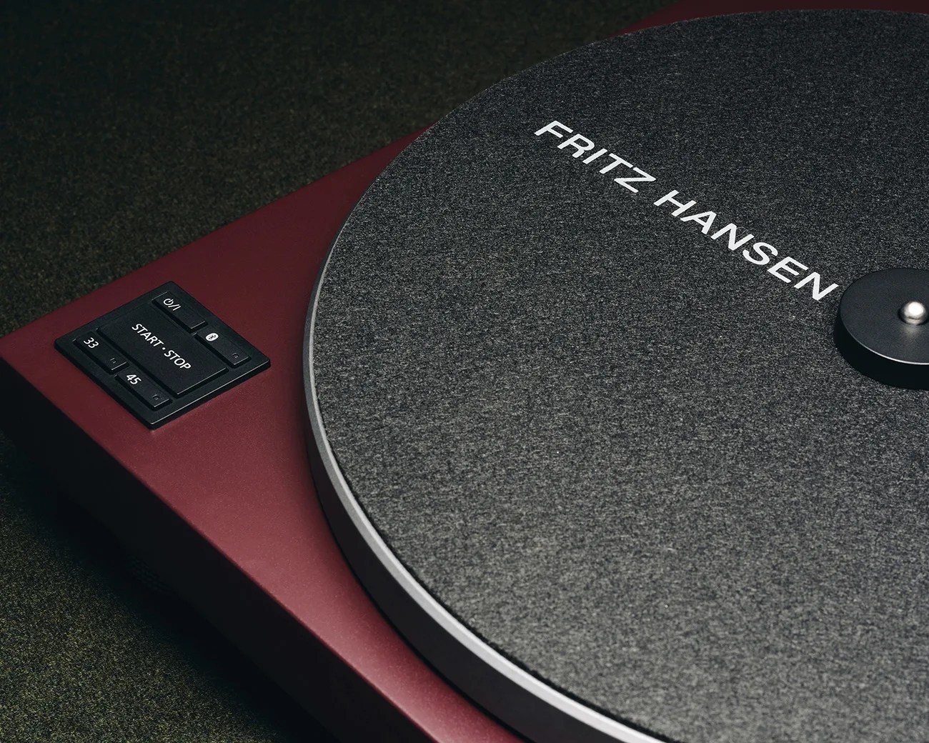 Close-up of a maroon Fritz Hansen turntable with a textured black platter and control buttons labeled start/stop, 33, and 45 RPM.