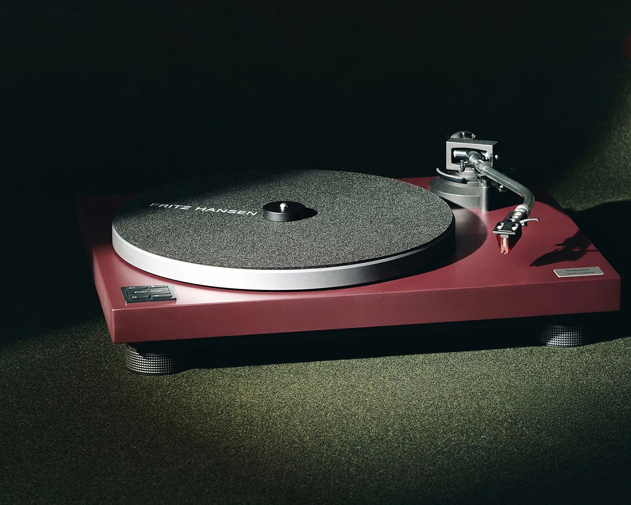 Burgundy Technics SL-1200MK2 turntable with black tonearm and gray felt platter mat labeled "Fritz Hansen.