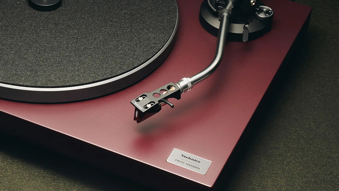Close-up of a burgundy Technics turntable with a black tonearm and a silver plaque labeled "Technics FRITZ HANSEN.