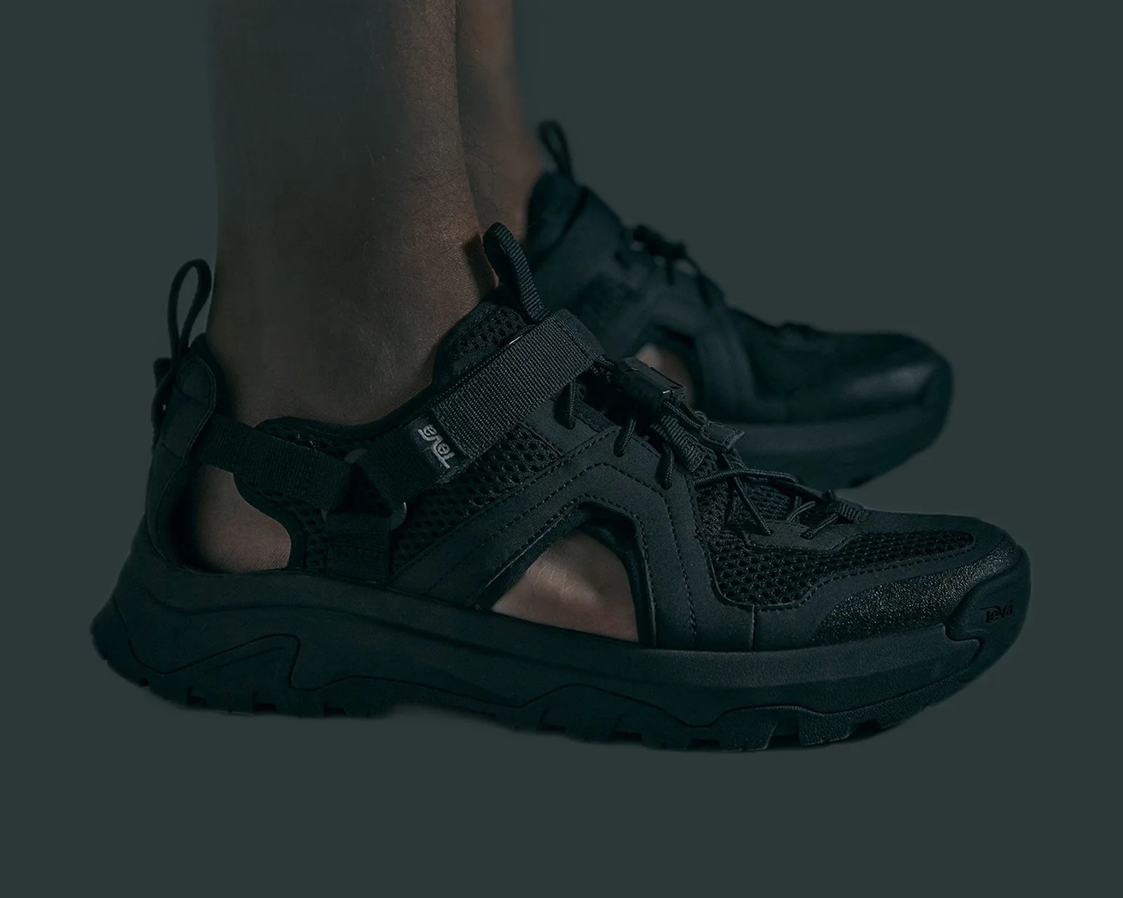 Black Teva sandals with mesh and synthetic upper, adjustable straps, and thick rugged sole worn on feet.