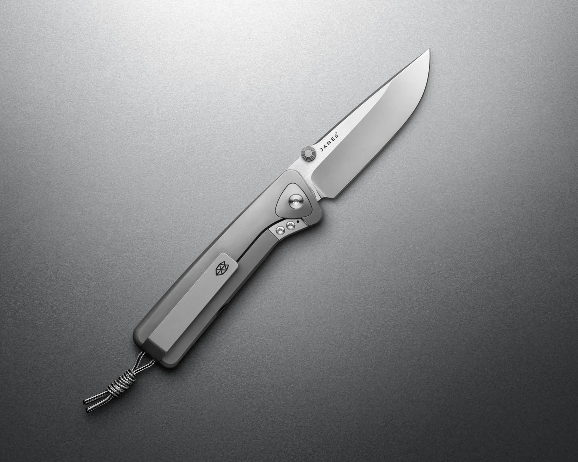 Silver folding knife with a smooth blade and a lanyard attached to the handle on a gray surface.