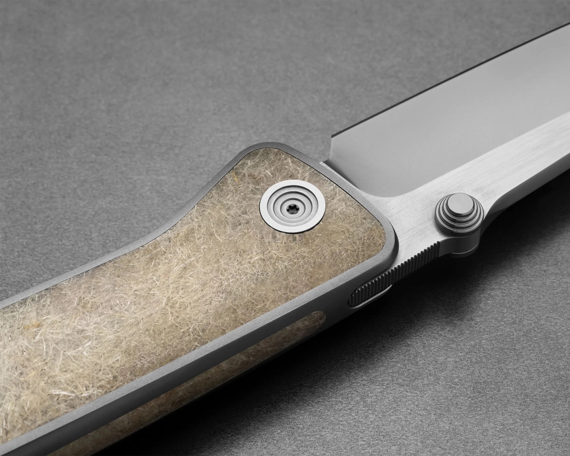 Close-up of a folding knife with a textured beige handle and a silver blade on a gray surface.