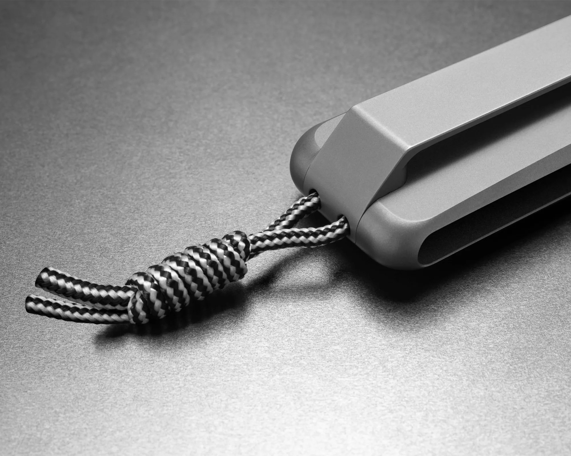 Matte gray metal device with a black and white braided cord attached, resting on a gray surface.