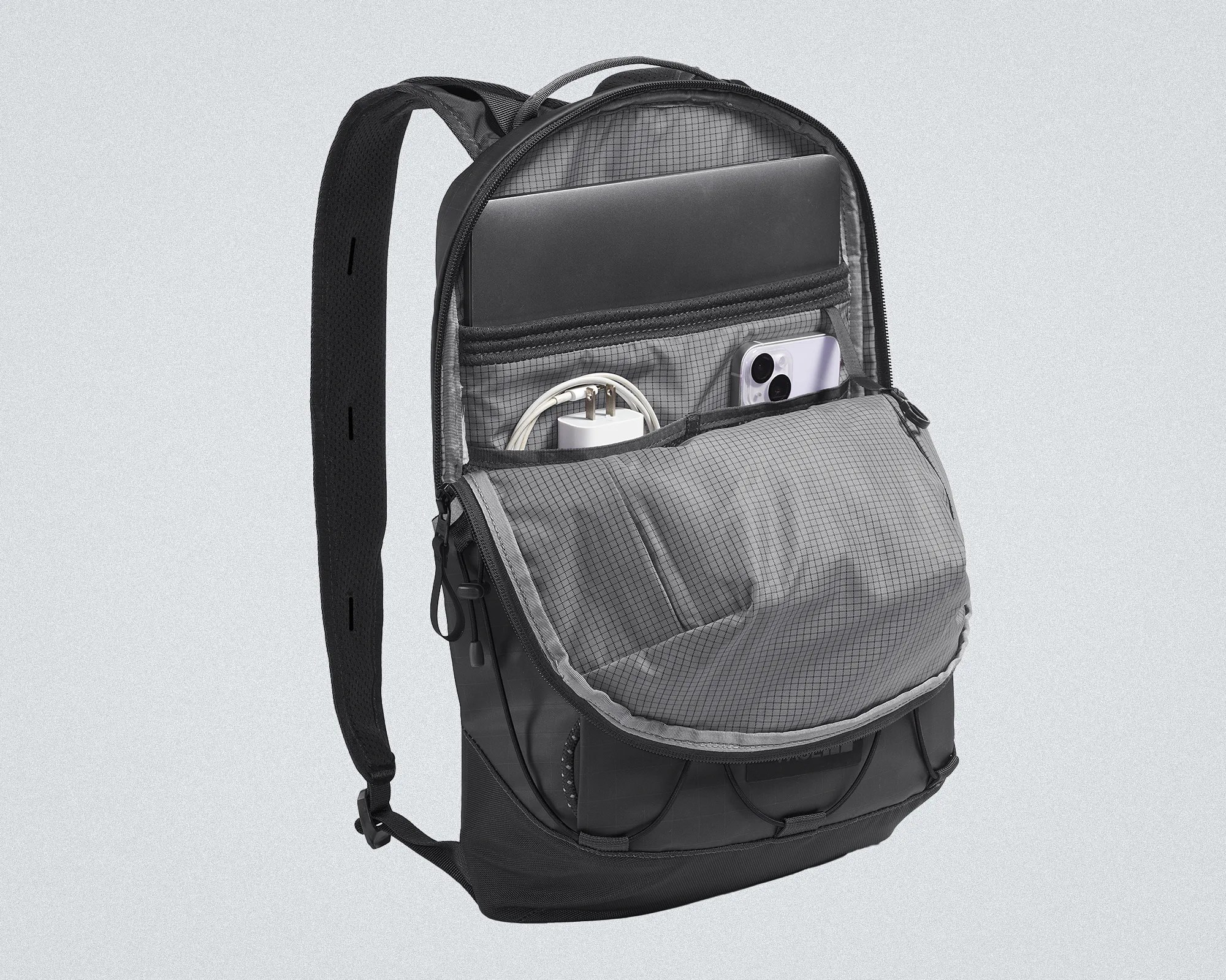 Black backpack with padded straps, open front compartment showing a laptop, phone, and charger inside.