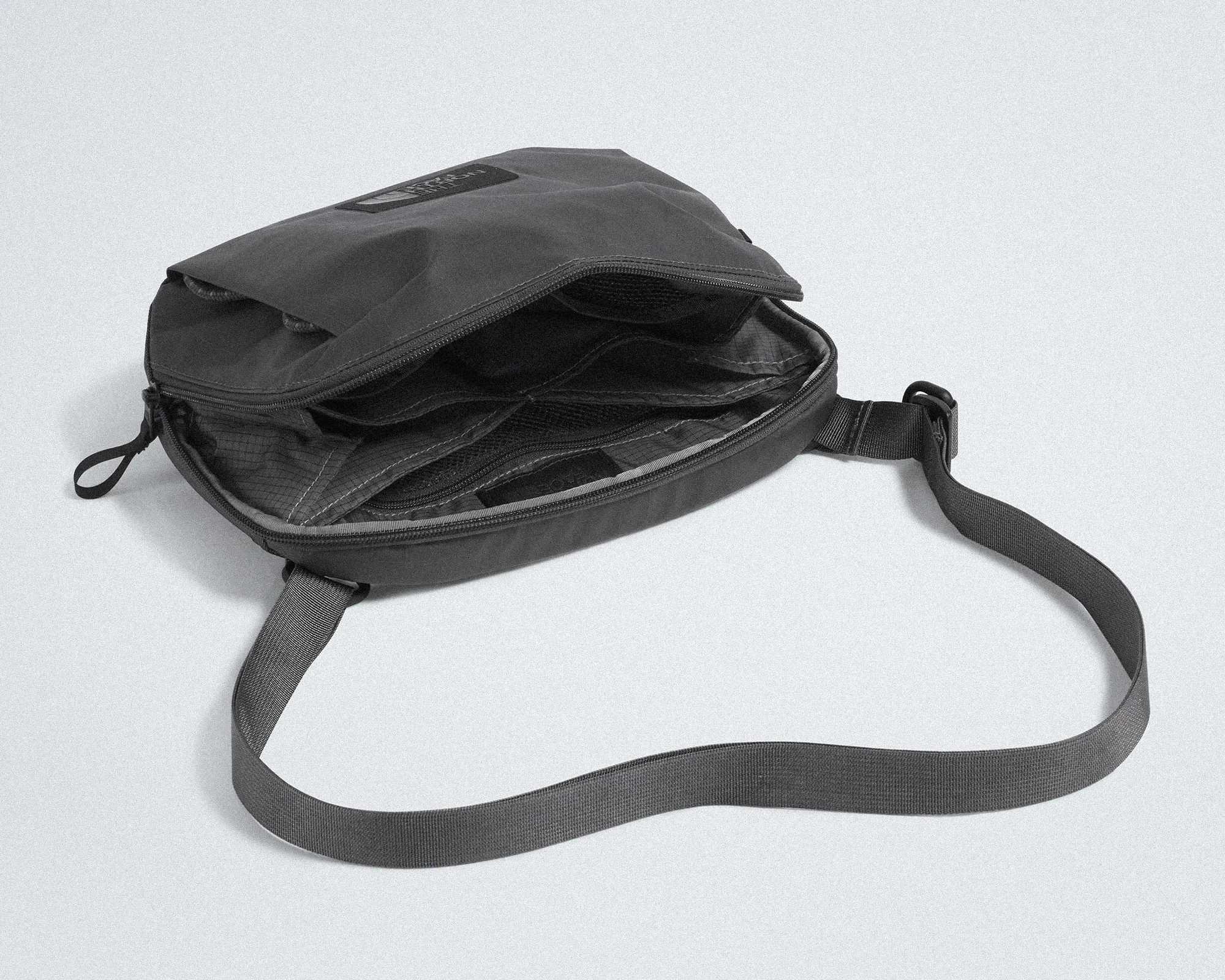 Black crossbody bag with multiple zippered compartments and adjustable strap on a white surface.