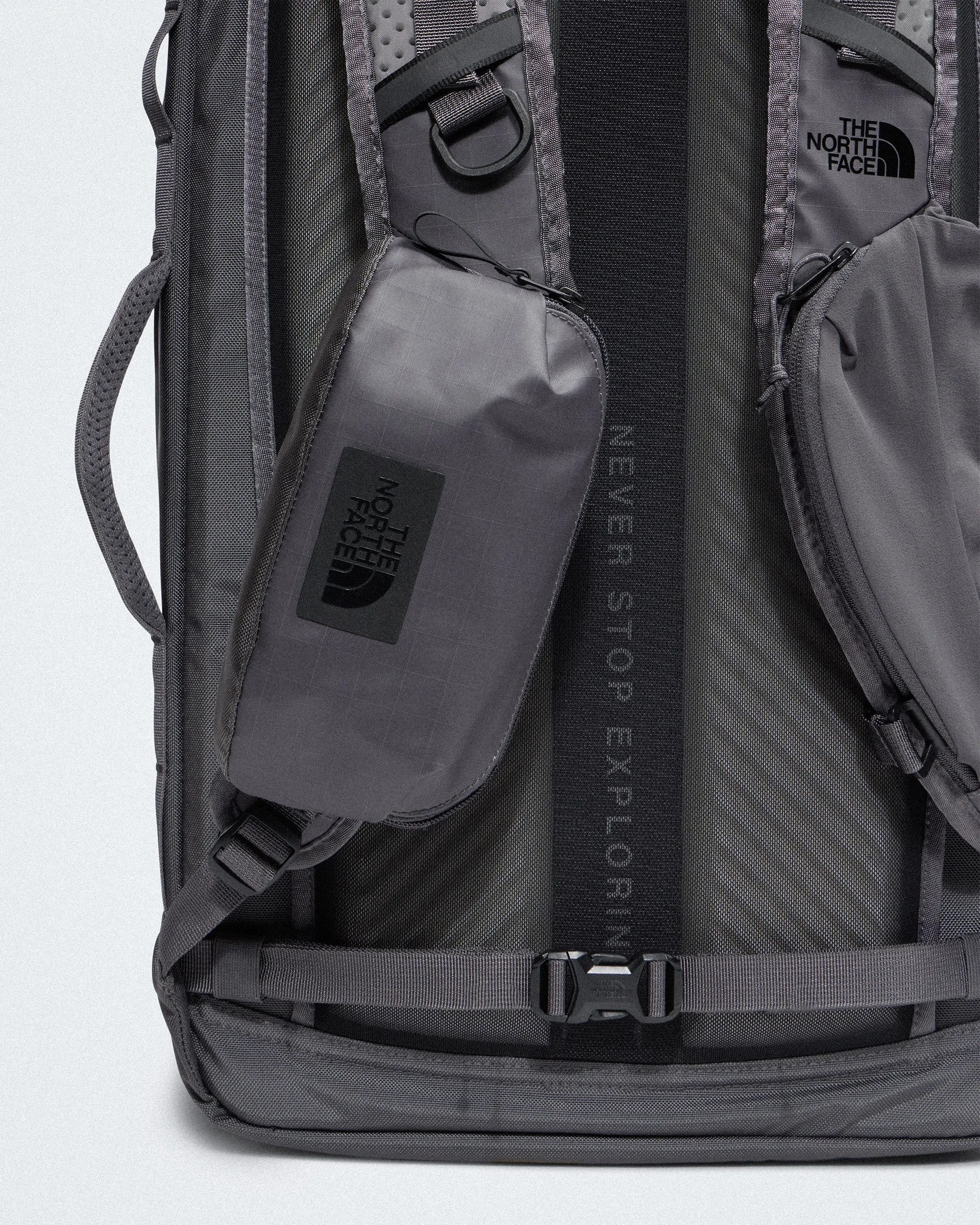 Close-up of gray The North Face backpack straps with attached zippered pouches and black buckle.