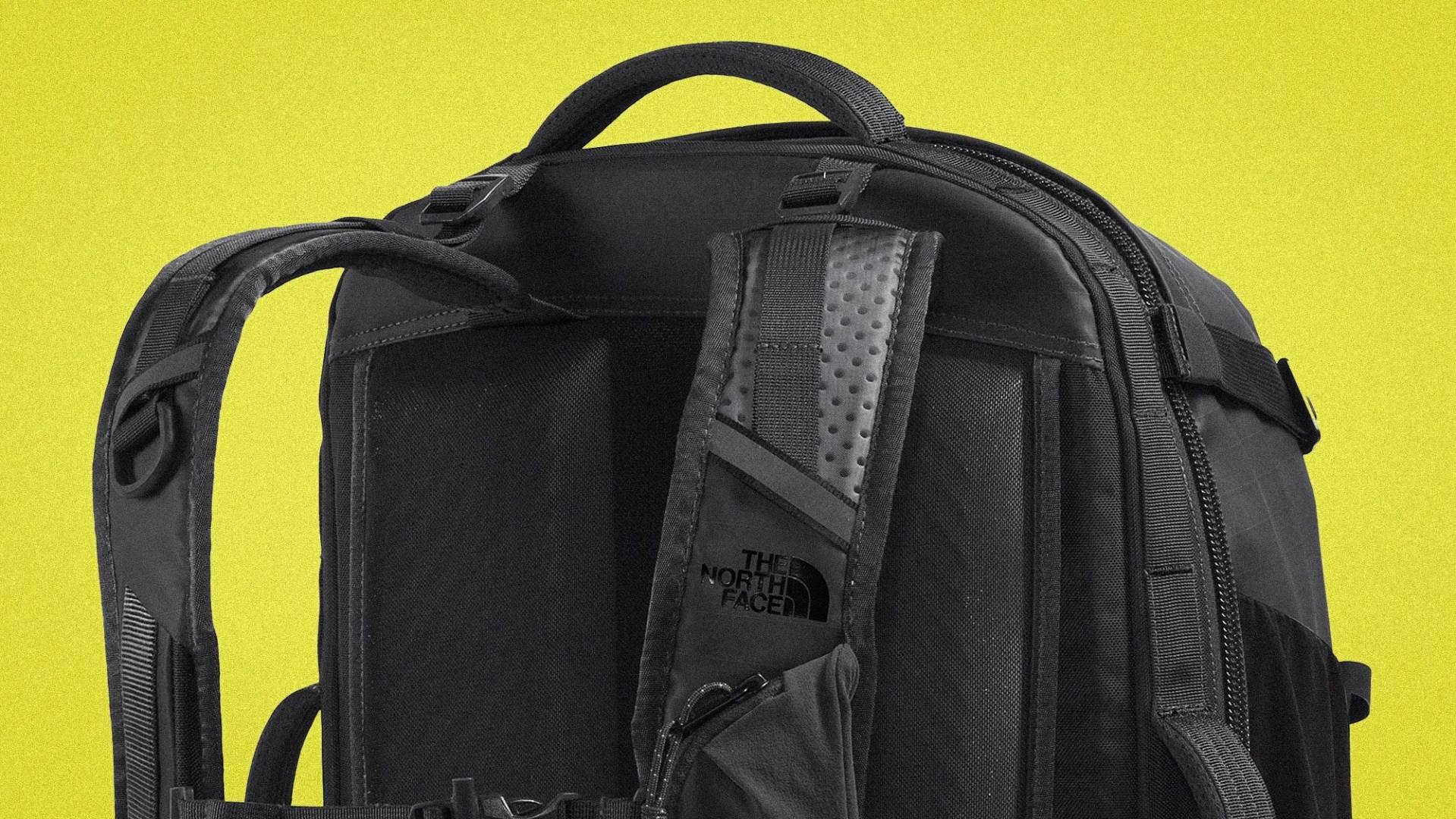 Black North Face backpack with padded shoulder straps and top handle against a yellow background.