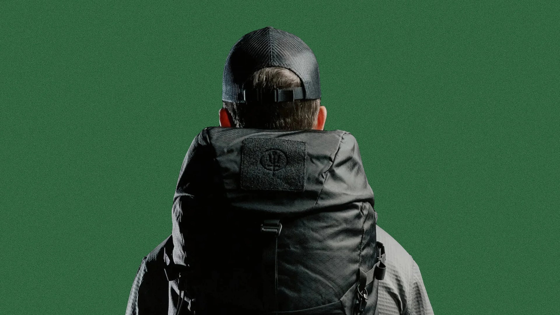 Person wearing a black textured backpack and black mesh cap facing away against a green background.