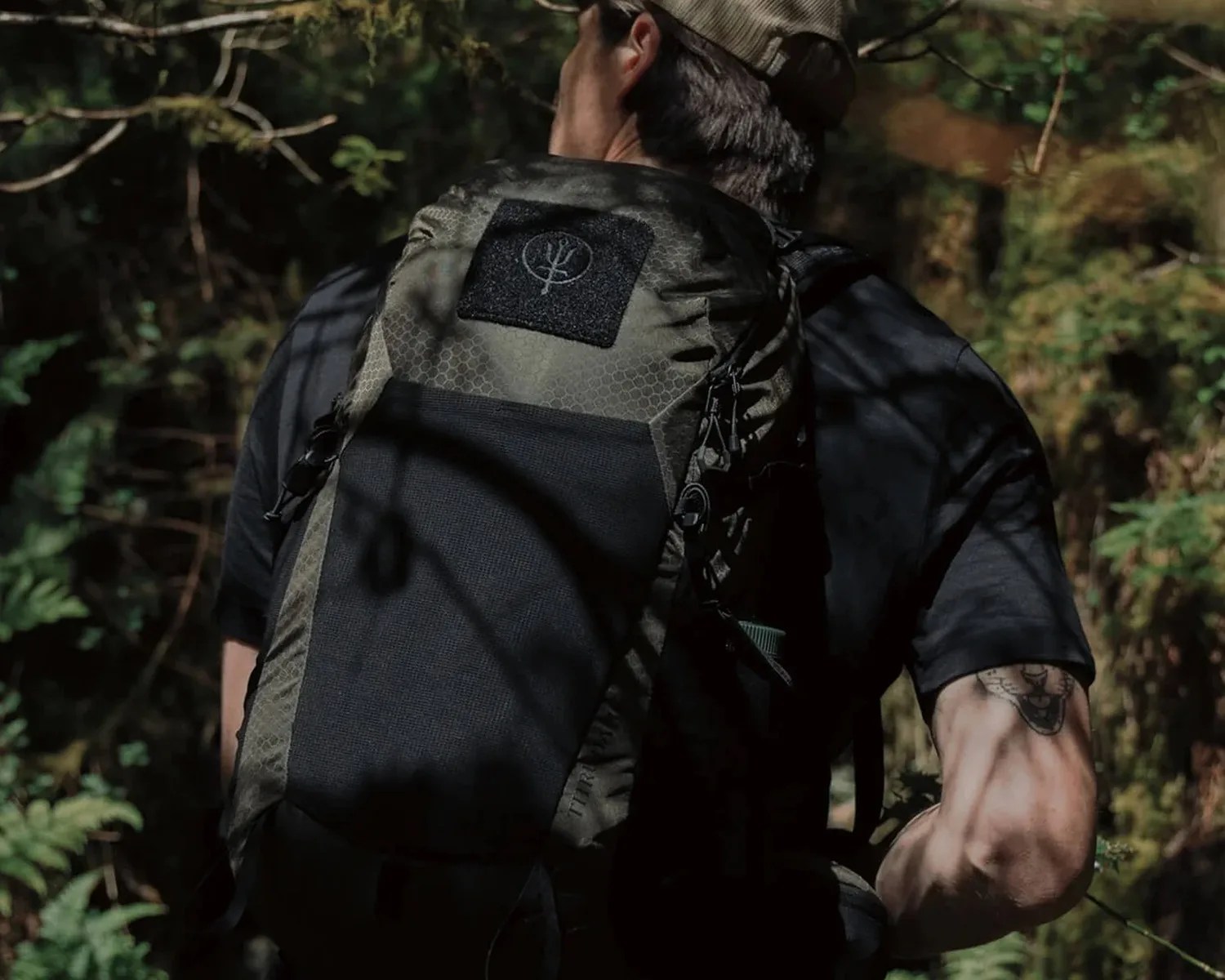 Olive green and black tactical backpack with hex pattern worn by a person in a forest.