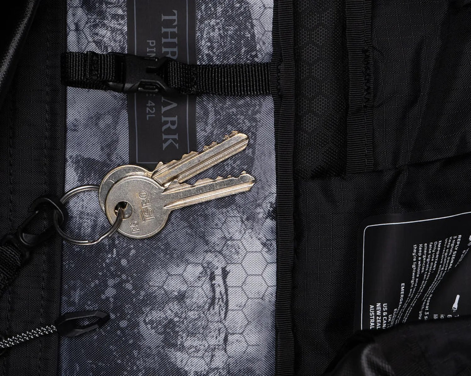 Two silver keys on a keyring attached to a black strap inside a black and gray backpack.