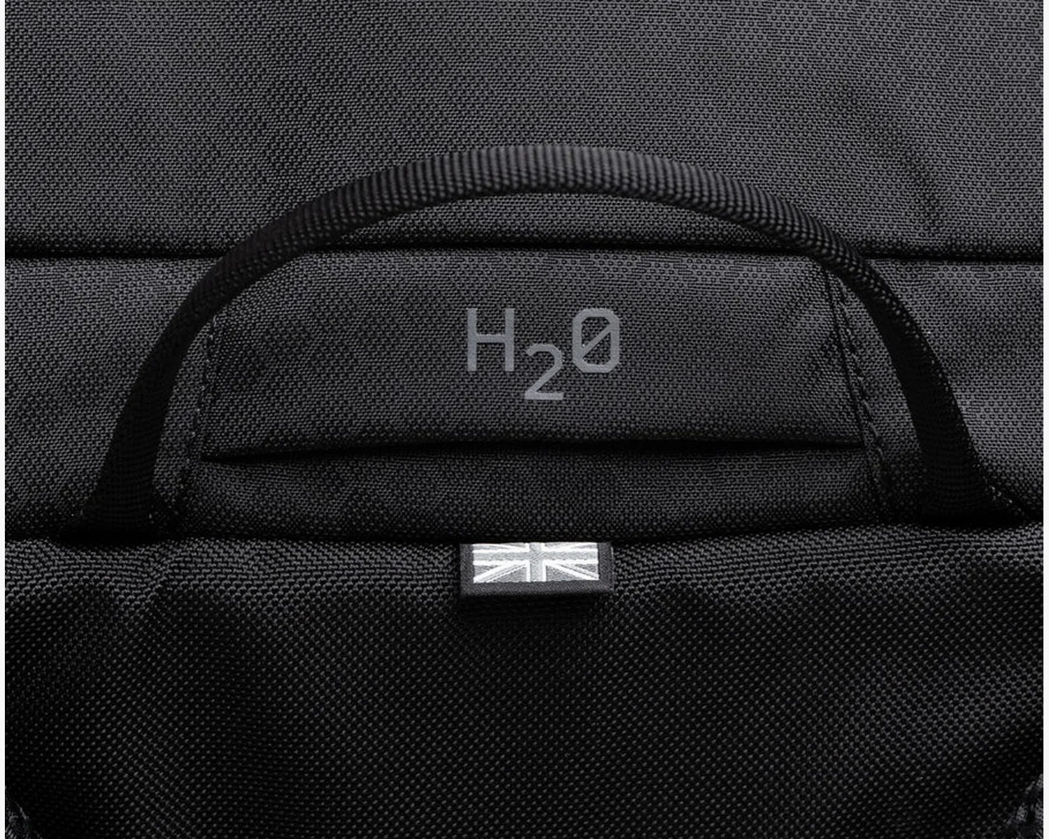Black textured fabric backpack with a top handle and "H2O" printed above a small Union Jack tag.
