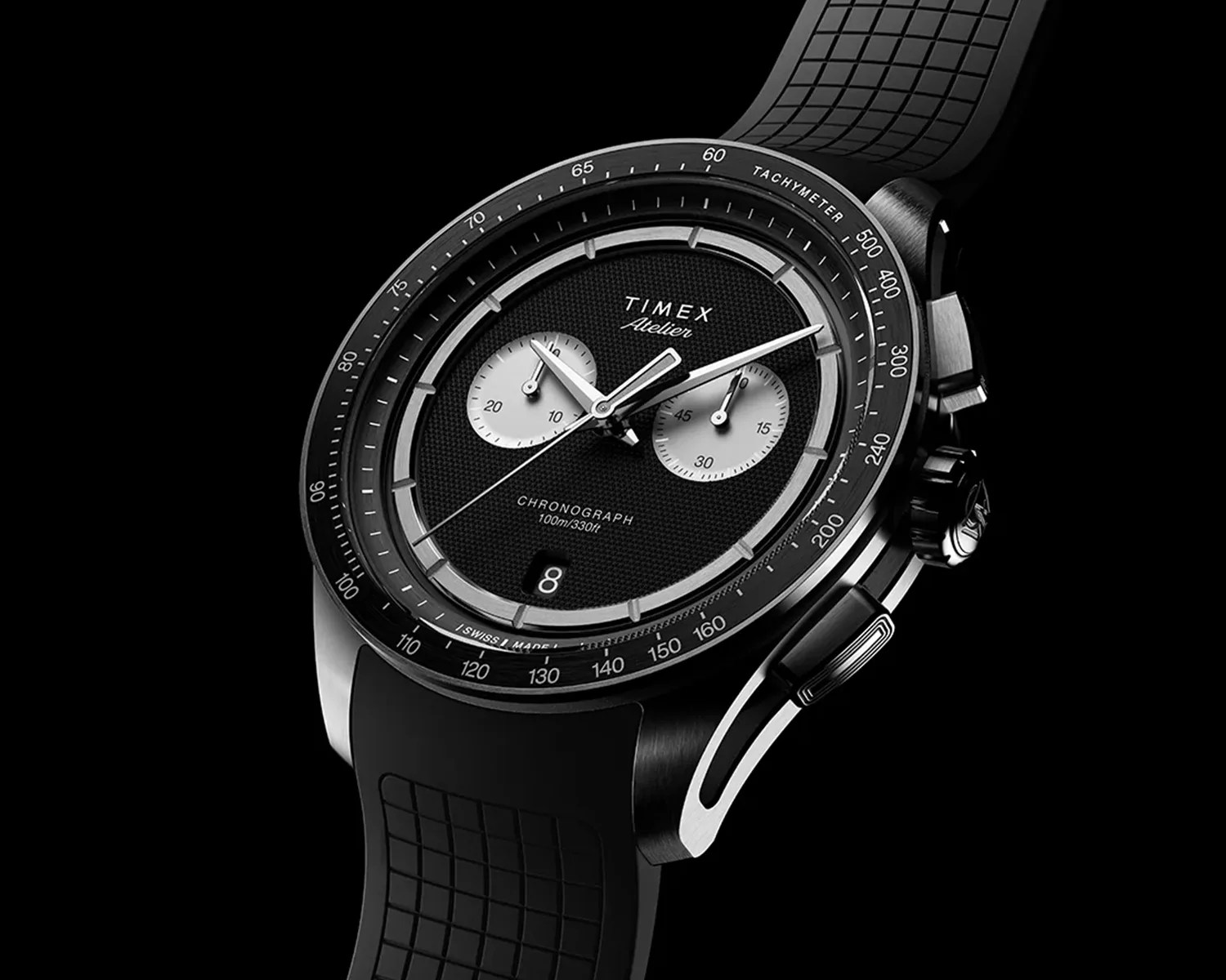 Black Timex Atelier chronograph watch with textured dial, two subdials, date window, and black rubber strap.