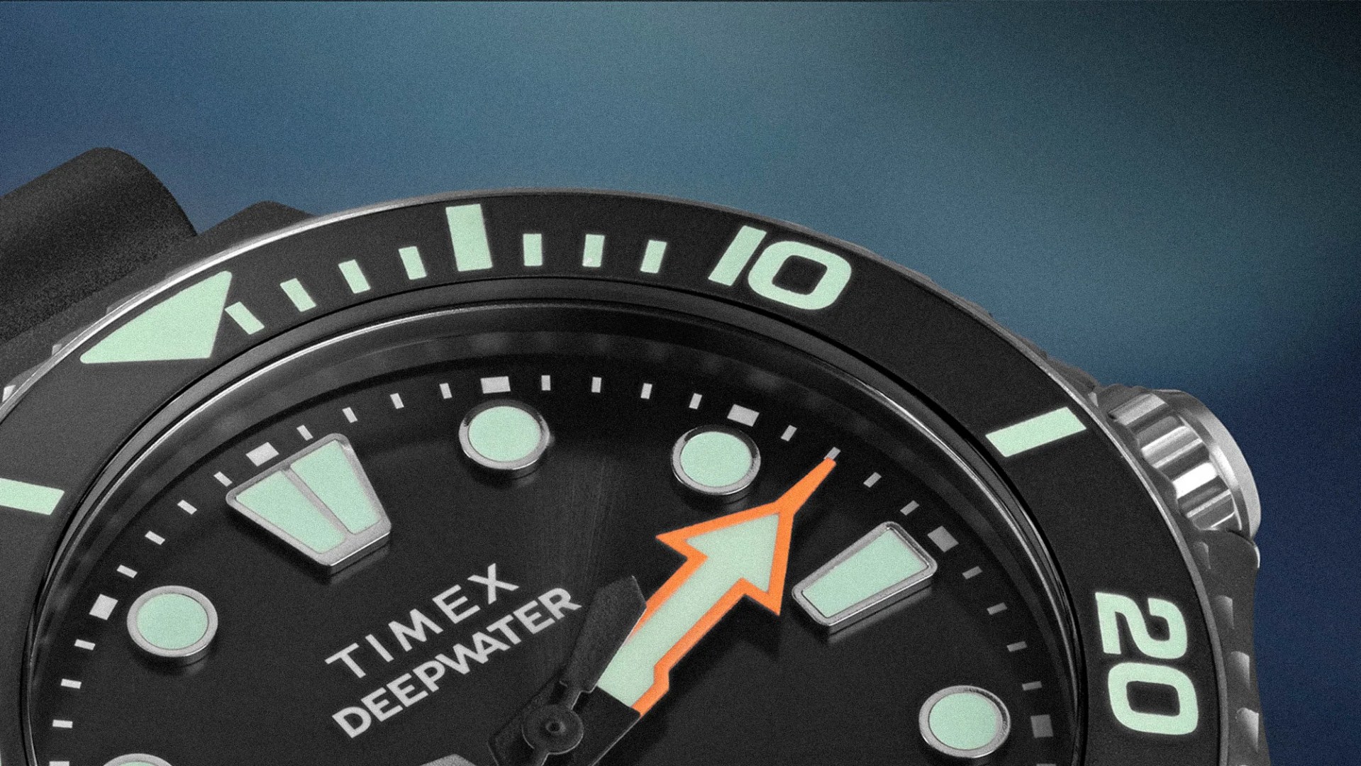 Close-up of a black Timex Deepwater watch face with luminous markers and an orange arrow-shaped hand.