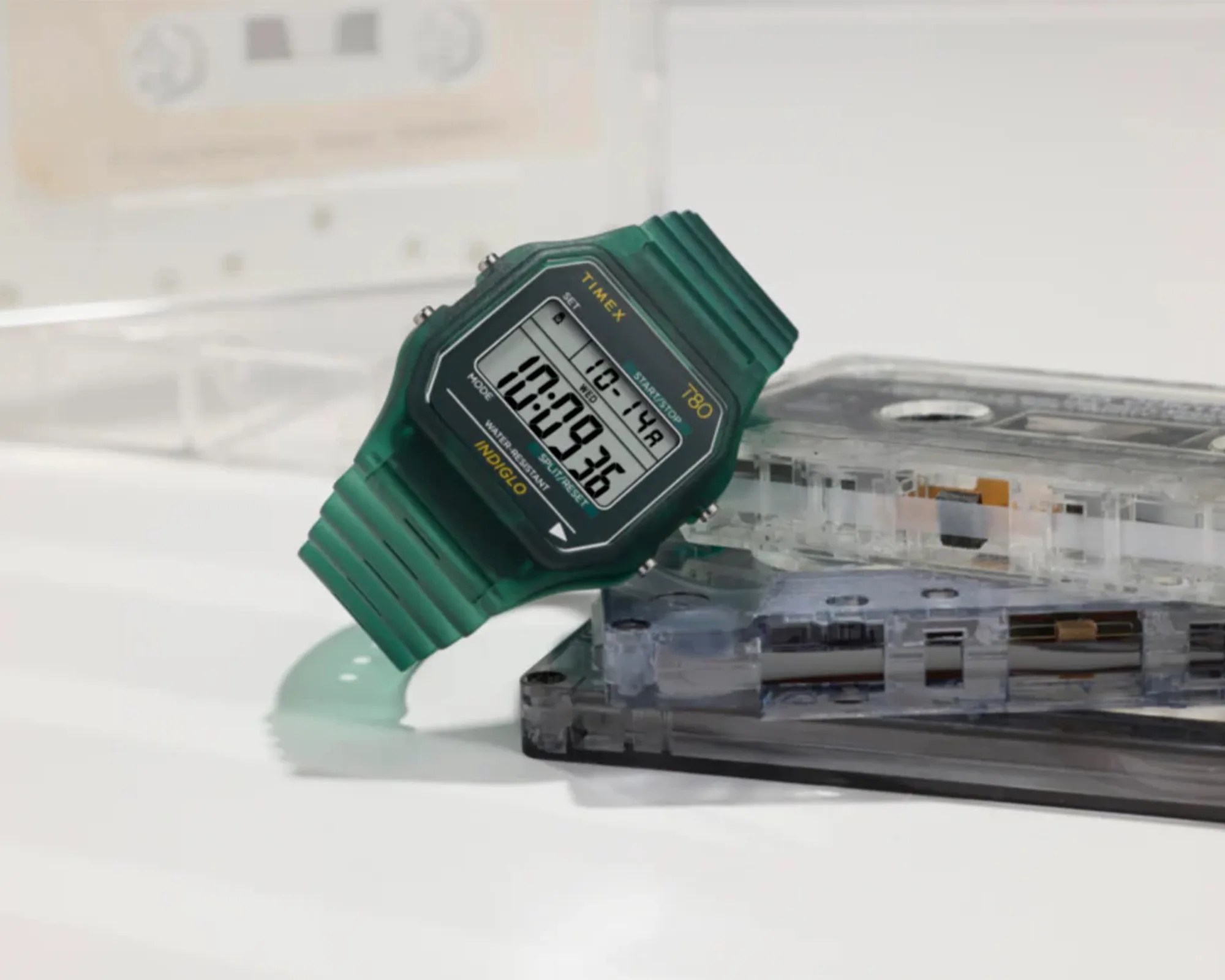 Green Timex T80 digital watch with black face and yellow text resting on clear cassette tapes.