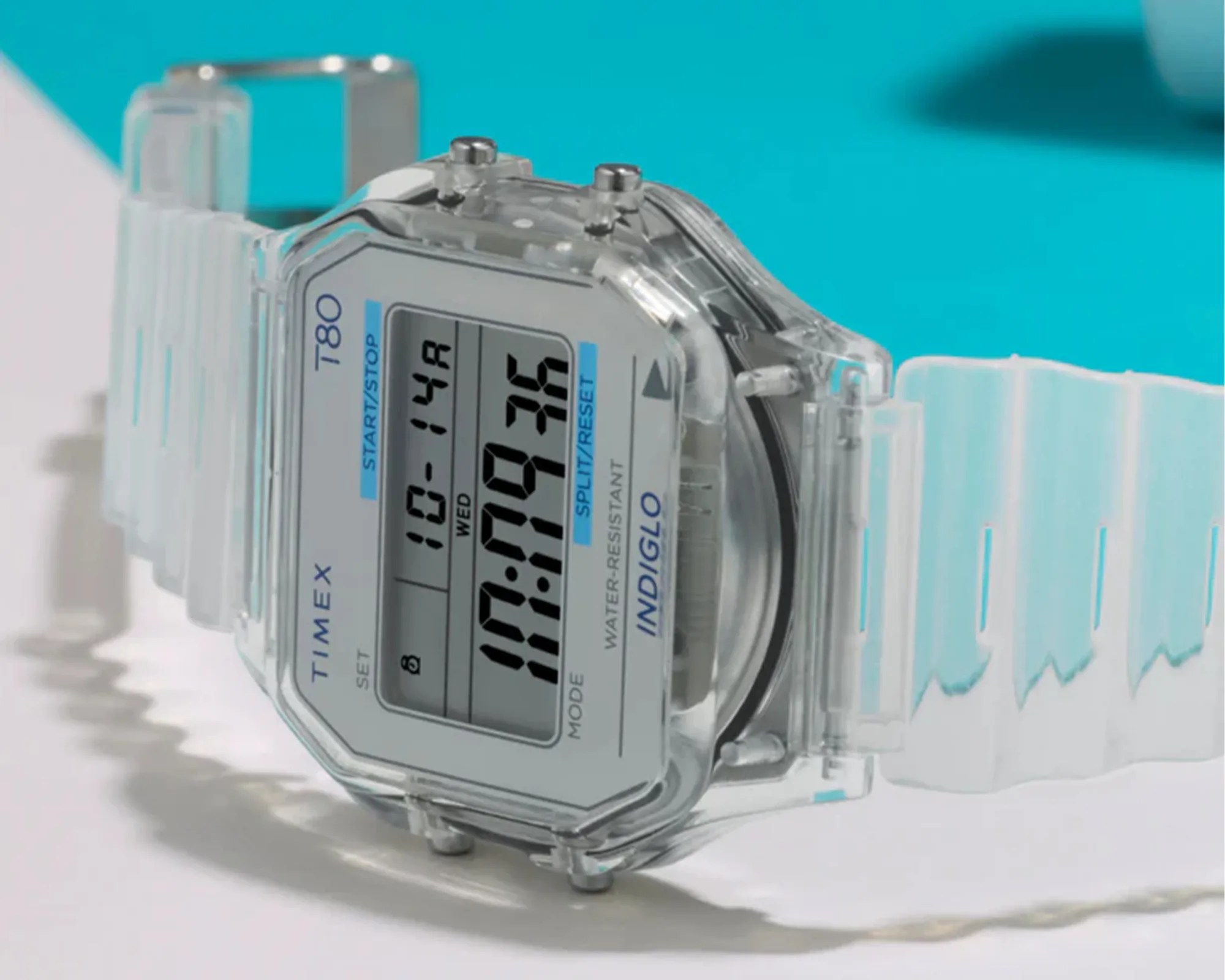 Transparent digital Timex T80 watch with a clear plastic strap on a white surface.