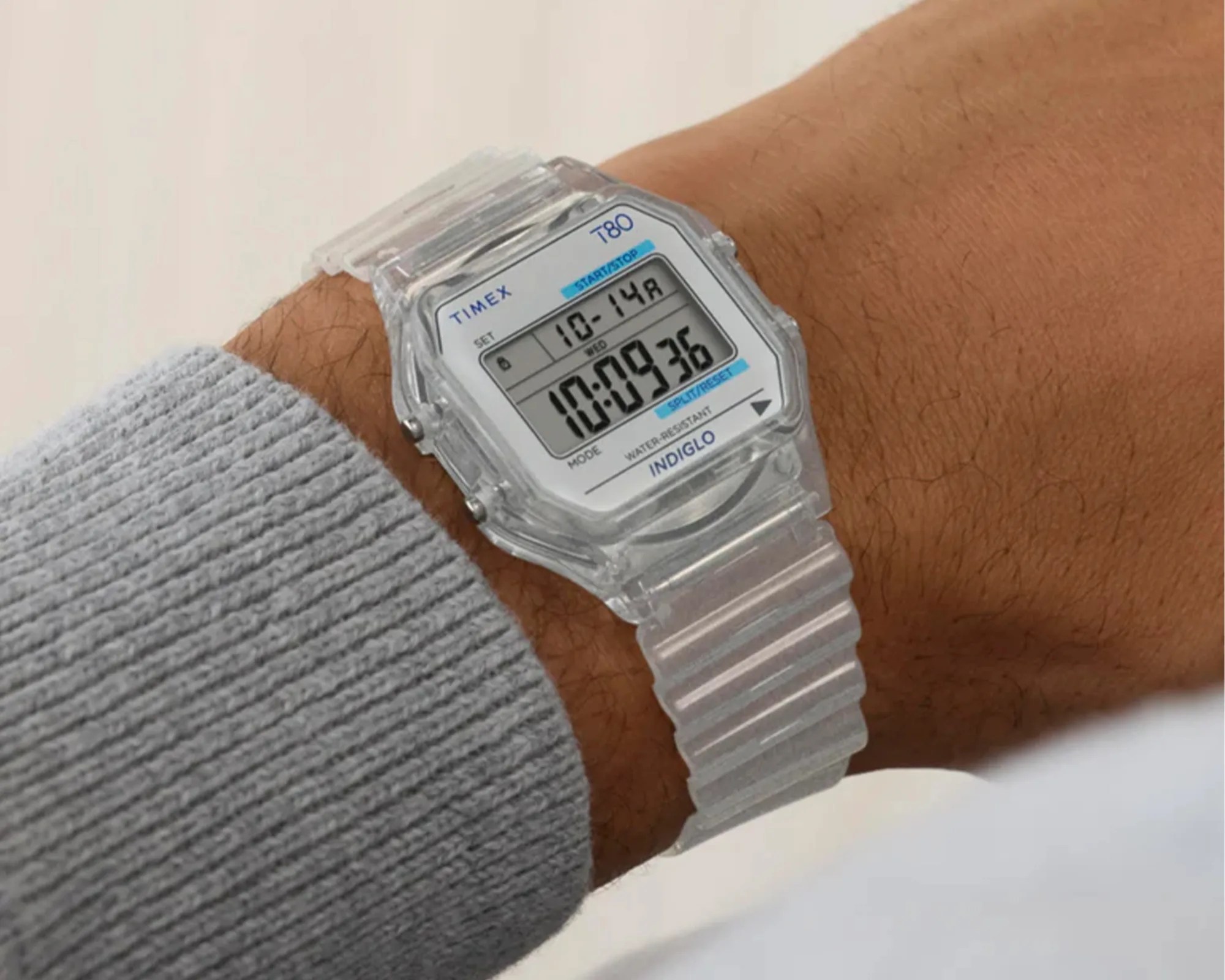 Clear plastic Timex T80 digital watch with a rectangular face showing date and time on a wrist.