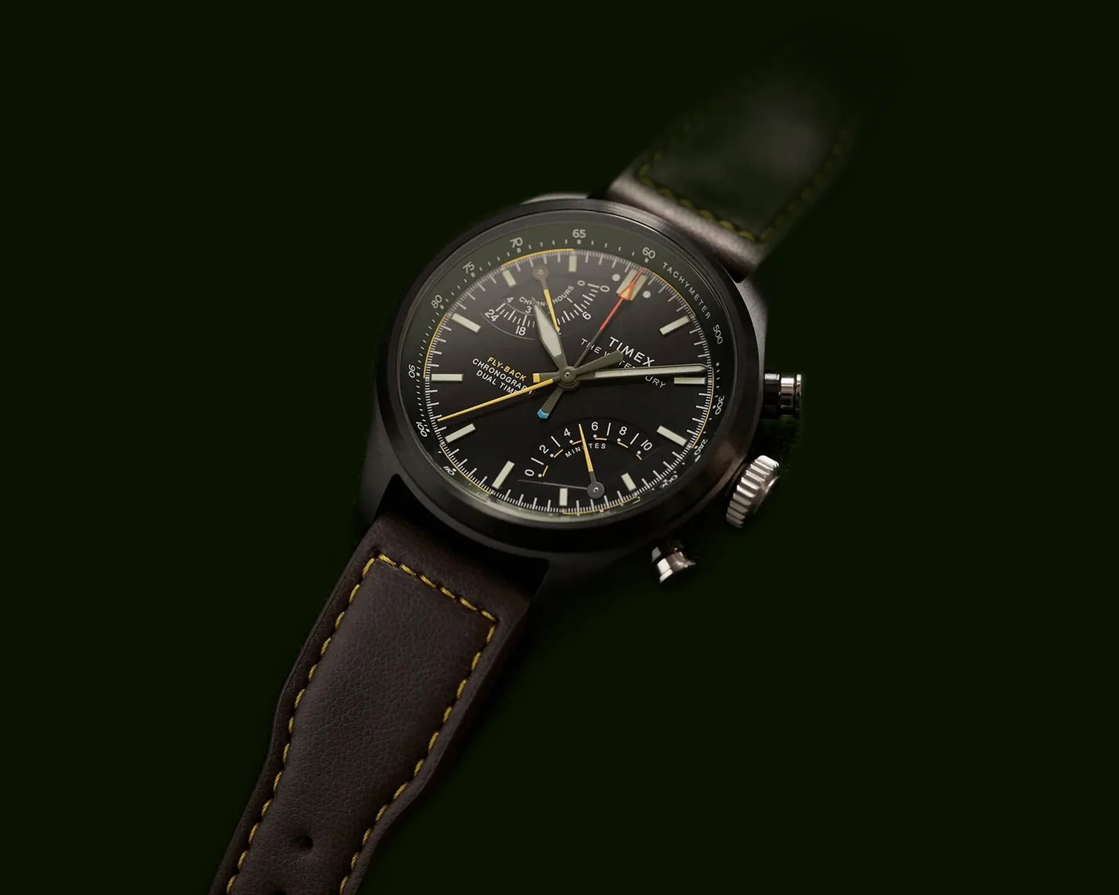Black Timex chronograph watch with yellow accents and brown leather strap with yellow stitching on a dark background.