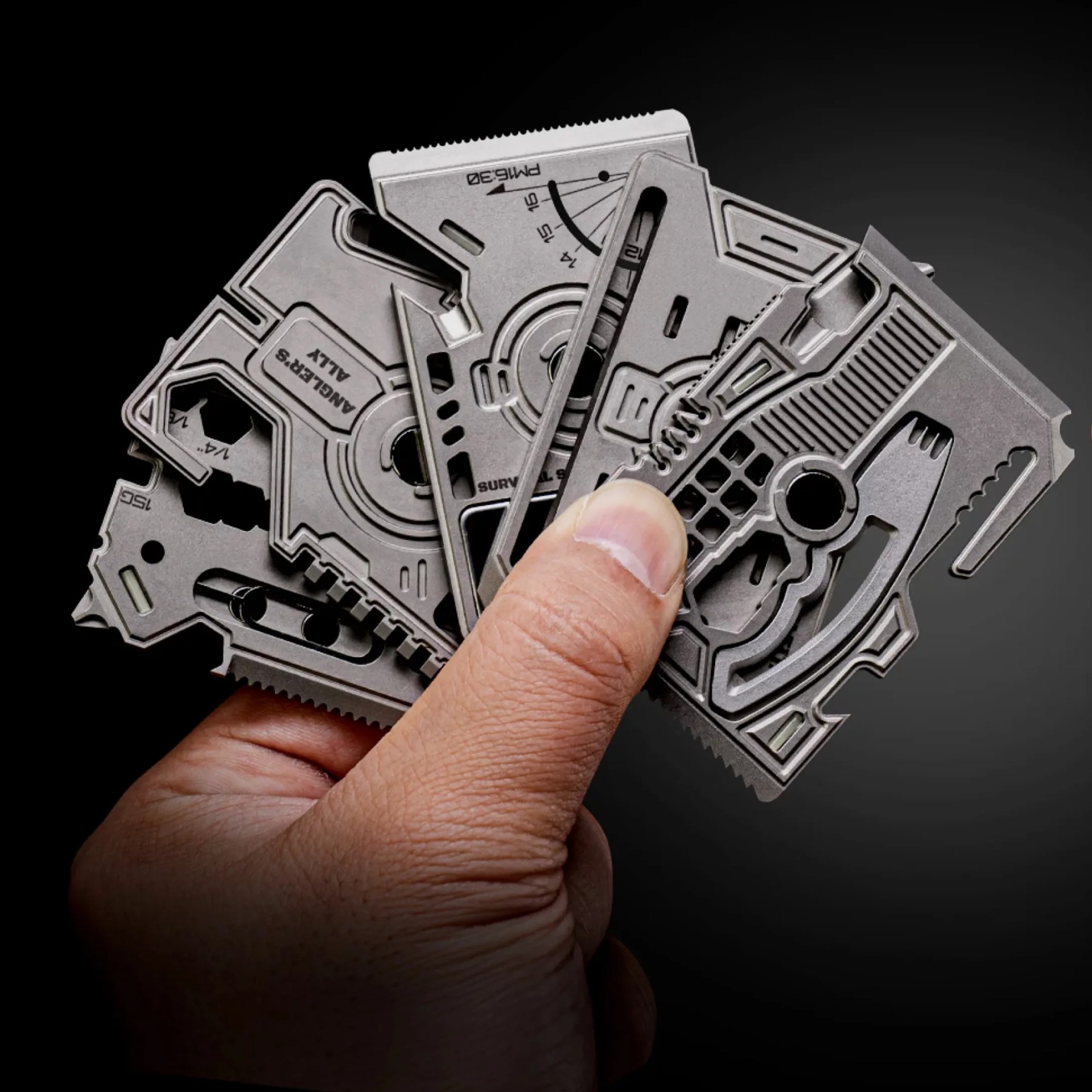 Hand holding a set of metal multi-tool cards with various cutouts and functions against a black background.