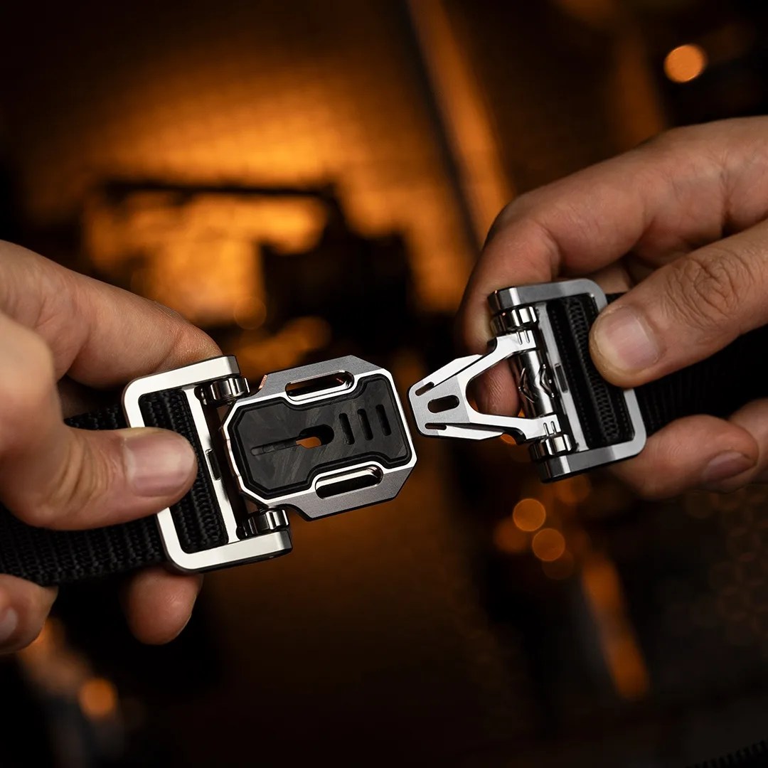 Close-up of hands holding a black nylon strap with a silver metal quick-release buckle.