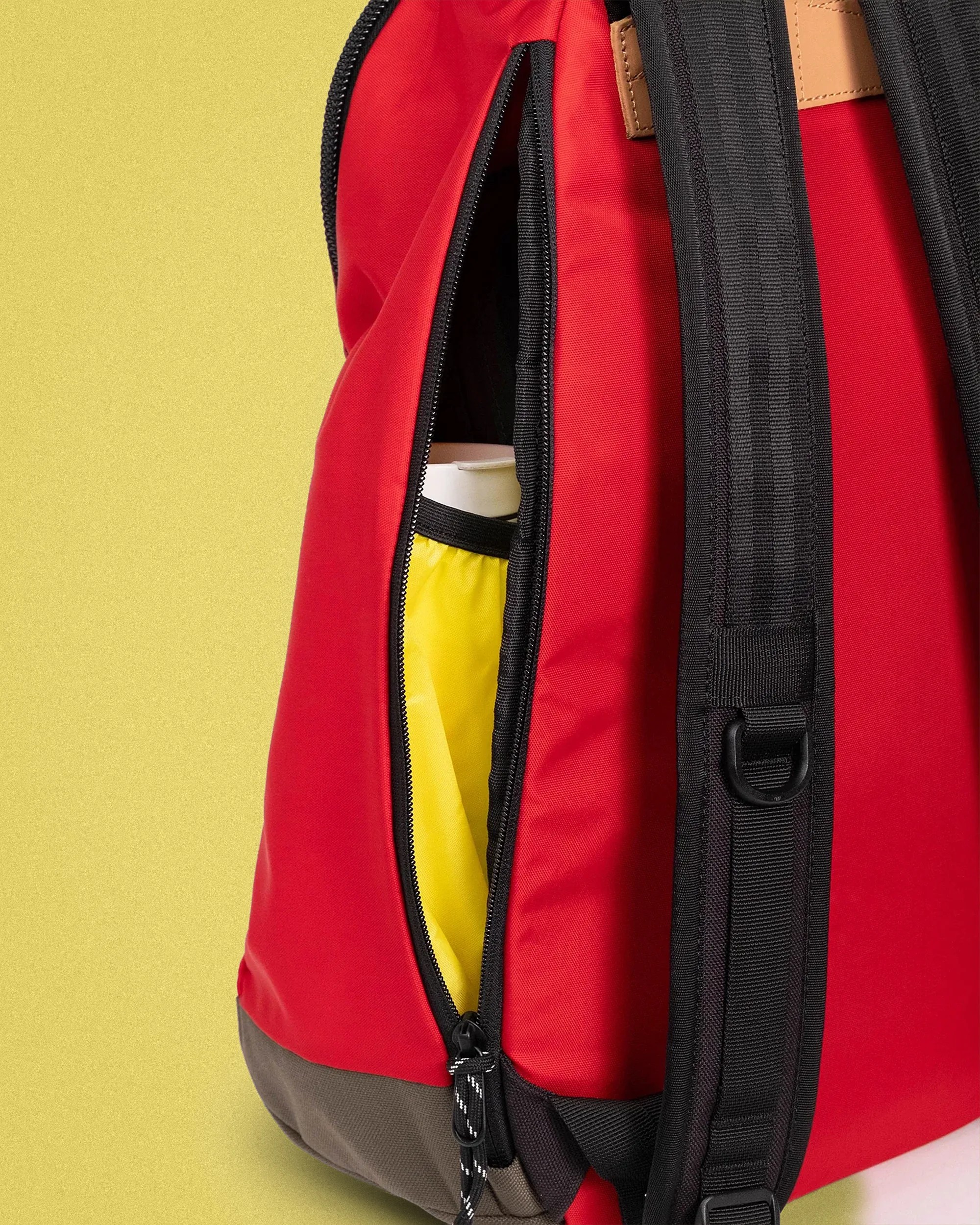 Red and gray backpack with black straps and a partially unzipped side pocket showing a yellow interior pouch.